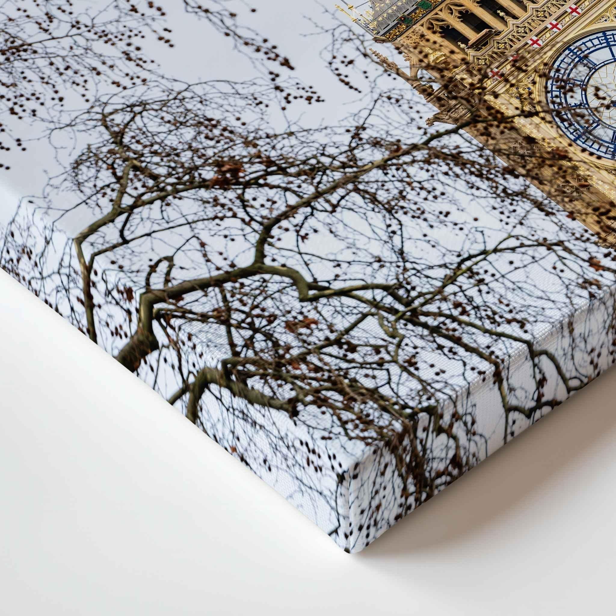 A close-up of a rectangular canvas print showing Big Ben, London with bare tree branches against a pale sky, with part of a golden building and a blue clock visible in the upper right. The product is photographed on a clean white surface.
