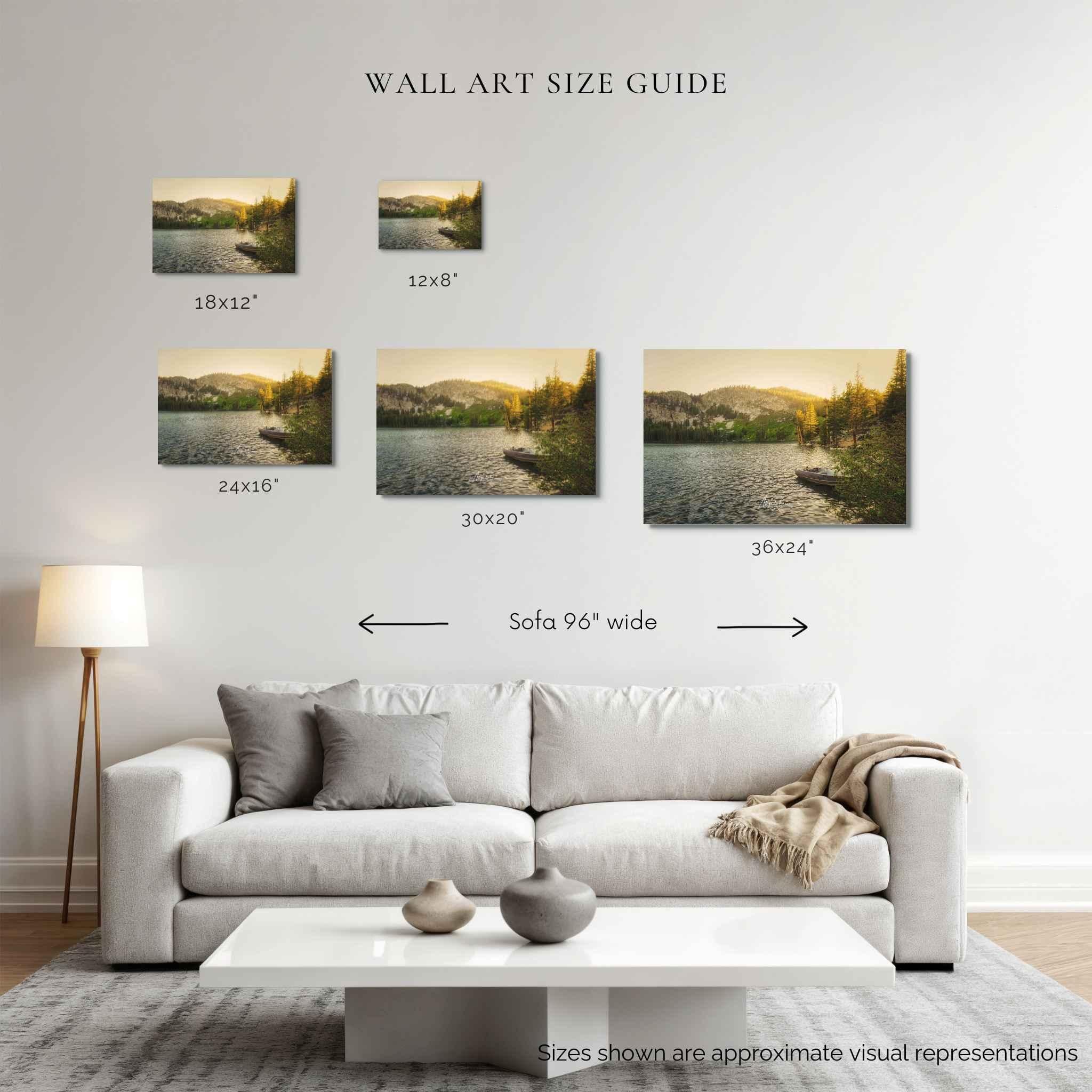 A wall art size guide displayed on a living room wall above a light gray sofa. The image shows five landscape canvas prints of golden hour at an alpine lake. labeled 18x12", 12x8", 24x10", 30x20", and 30x24", with text indicating sofa width 96" and approximate size representations.