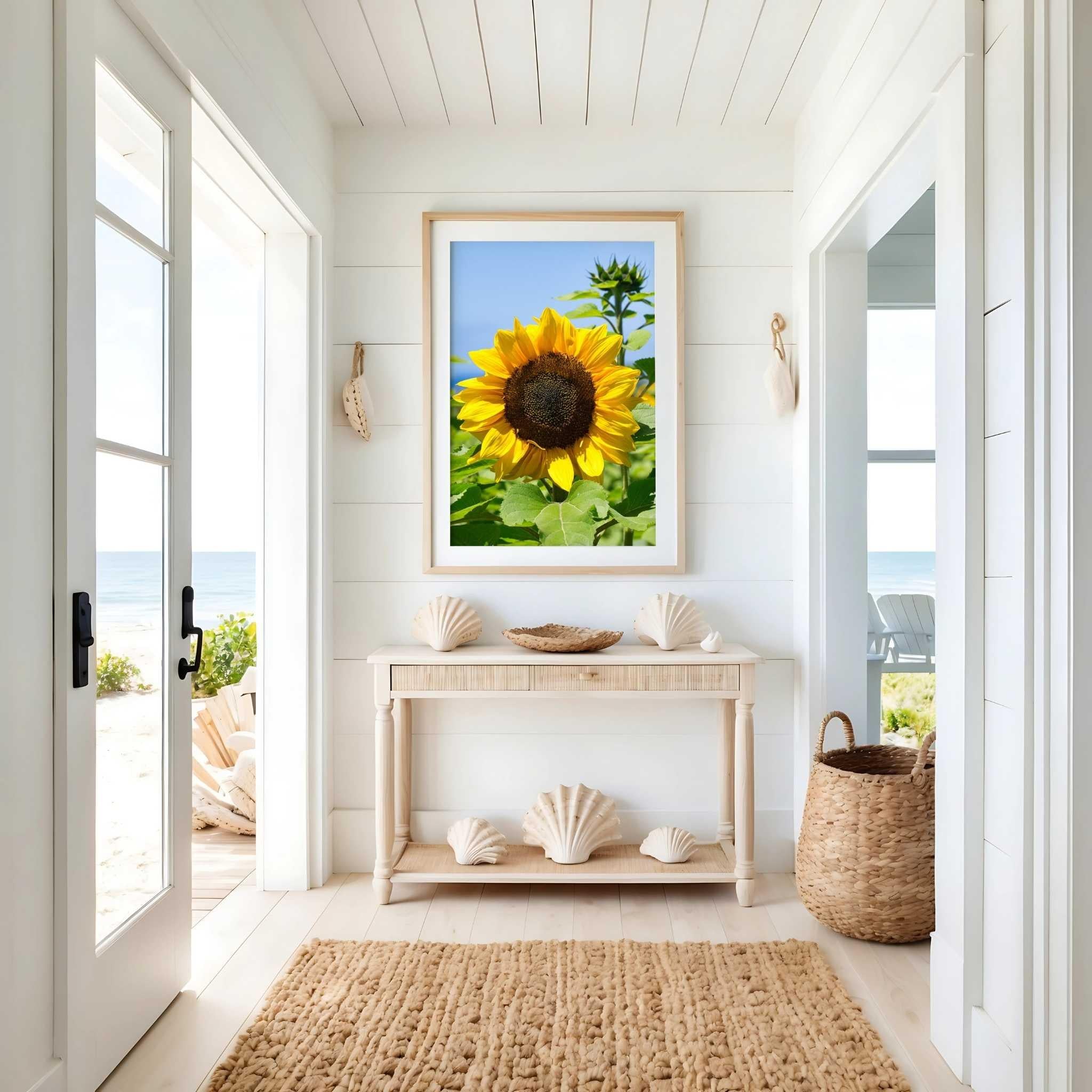 Turning Towards the Light sunflower wall art by Abigail Diane Photography displayed in a natural oak frame above a coastal console table with seashell décor in a bright California coastal beach house entryway.