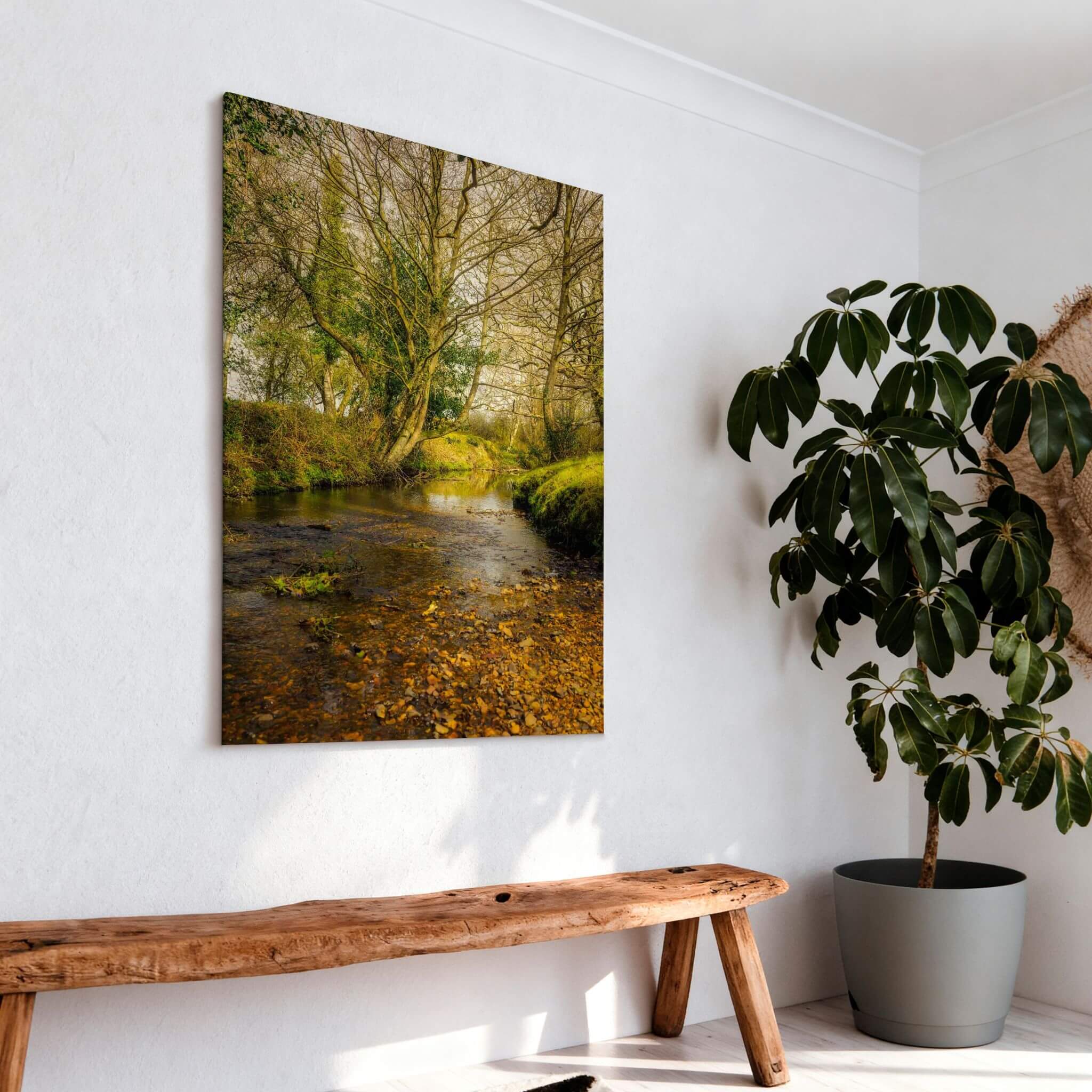 A Lazy Creek in the New Forest print displayed above a rustic wood bench in a bright natural interior with greenery.