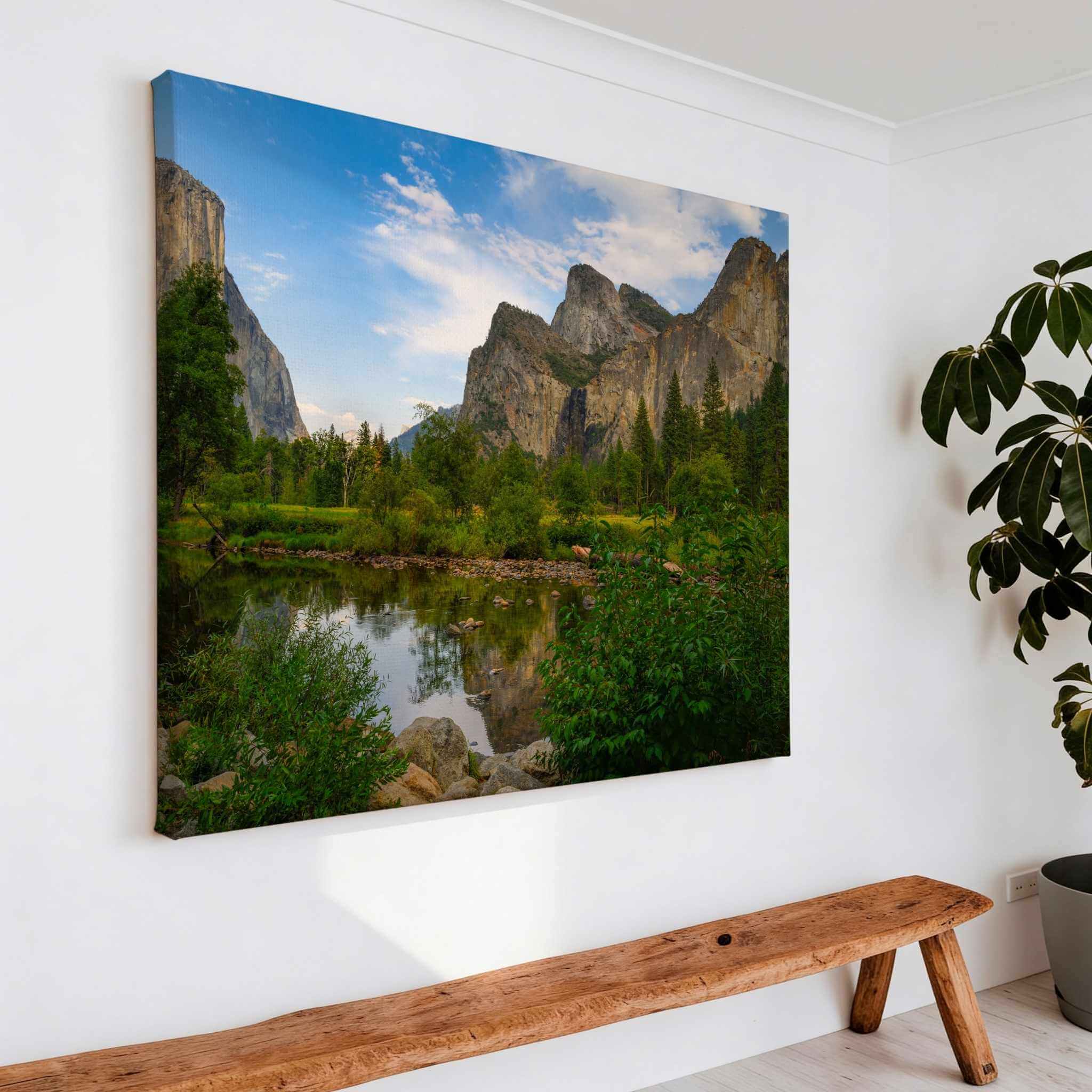 Large gallery-wrapped canvas featuring; A Majestic Day in Yosemite Valley, capturing Yosemite Valley's towering granite cliffs, peaceful river reflections, and lush green meadows in California, displayed above a handcrafted wooden bench in a bright modern entryway by Abigail Diane Photography.