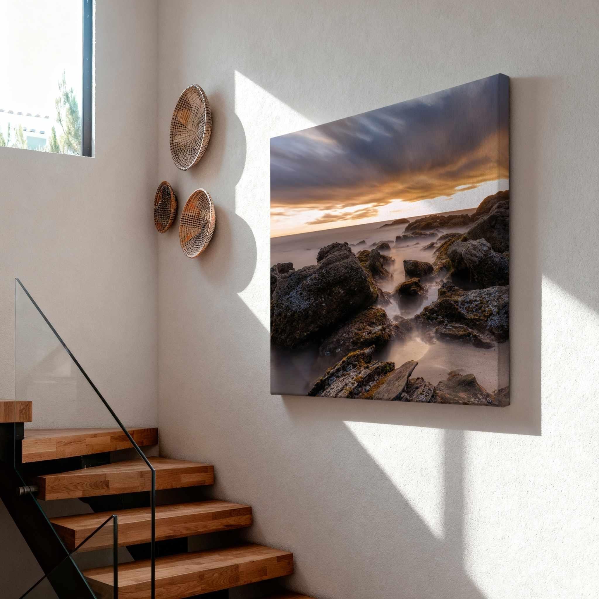 After the Storm gallery-wrapped canvas print displayed on a modern stairway wall, featuring a dramatic long exposure sunset over the rocky shoreline of Laguna Beach, California.