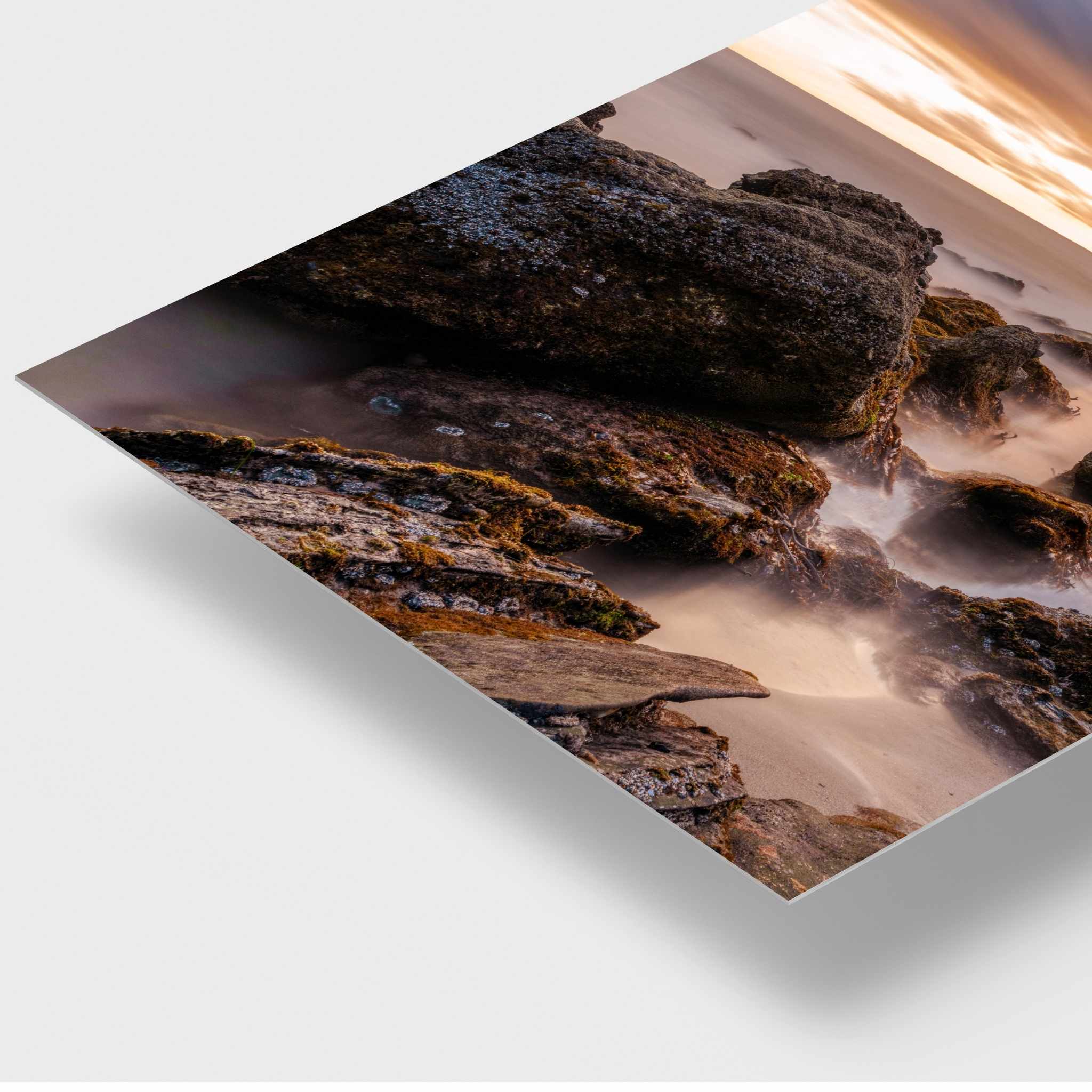 Close-up angled view of the After the Storm HD metal print by Abigail Diane Photography, showcasing the ultra-slim profile, glossy finish, and exceptional detail of moss-covered coastal rocks and flowing surf at Laguna Beach, California.