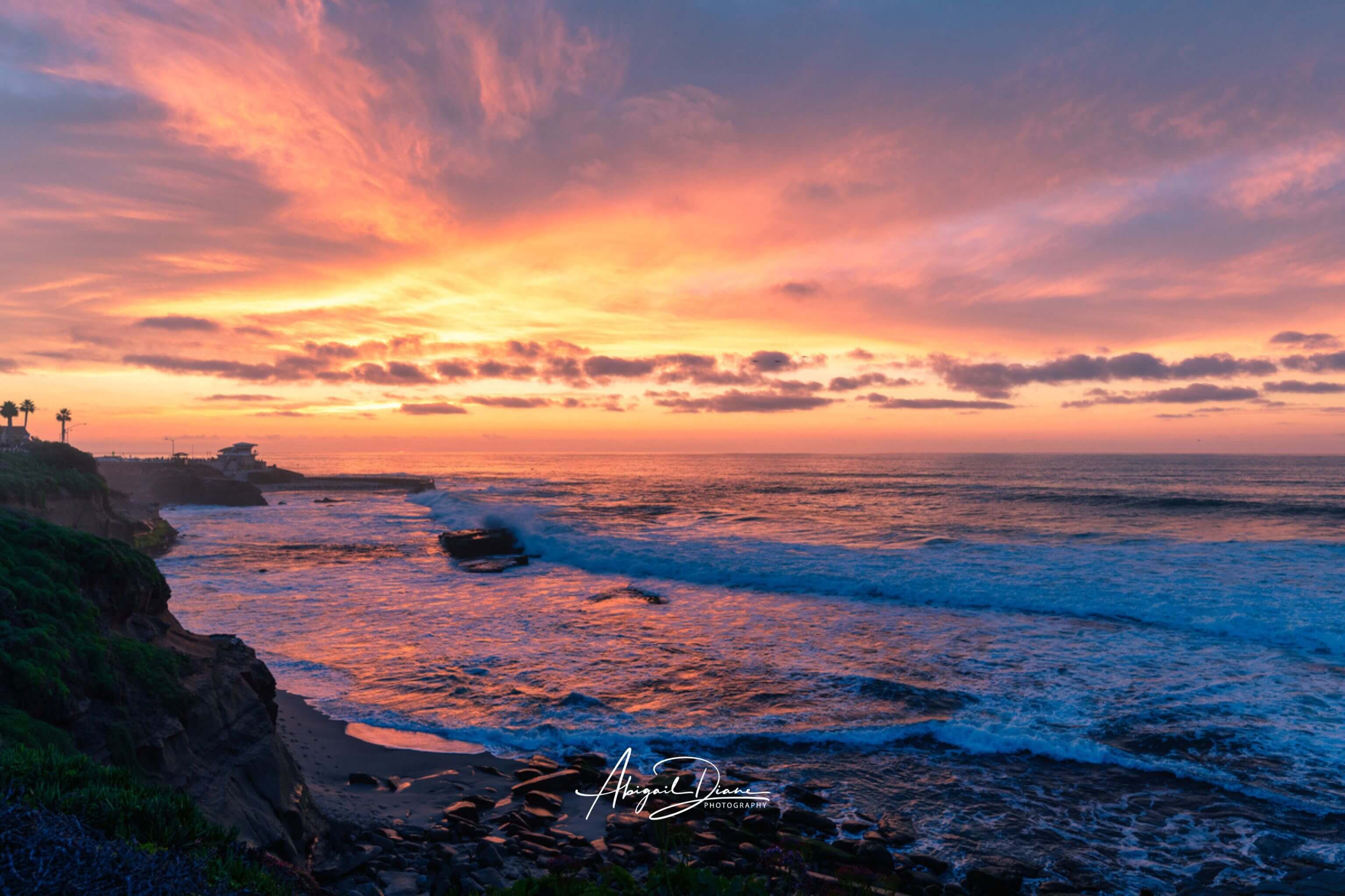 Candy floss pink, peach and lavender winter sunset glowing over the Pacific Ocean and rocky coastline in La Jolla, San Diego, California. Photography by Abigail Diane Photography.