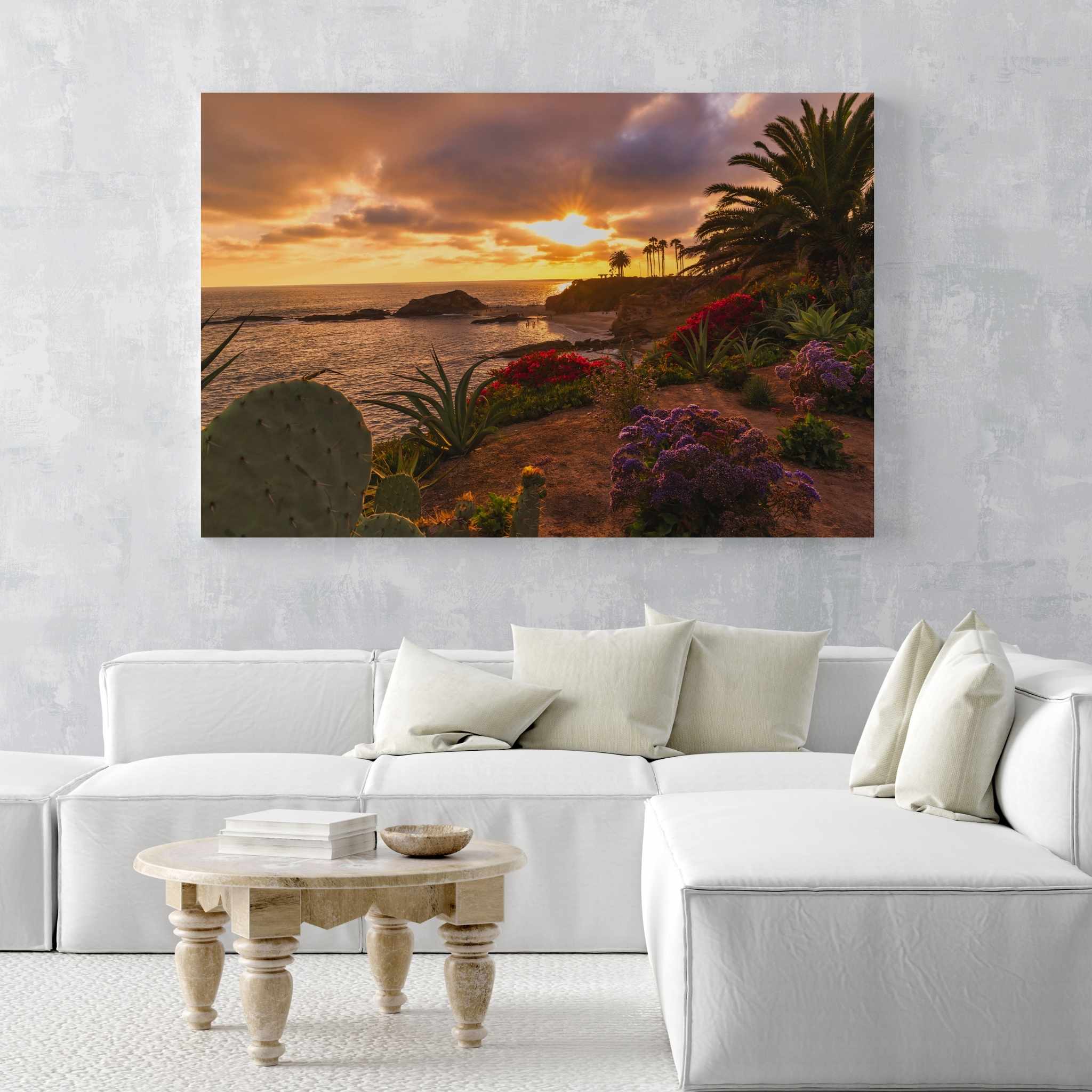 Large Basking in the Golden Sunset dye-sublimation metal print by Abigail Diane Photography displayed above a white sectional sofa, featuring a glowing Laguna Beach California sunset with colorful coastal gardens and ocean views.