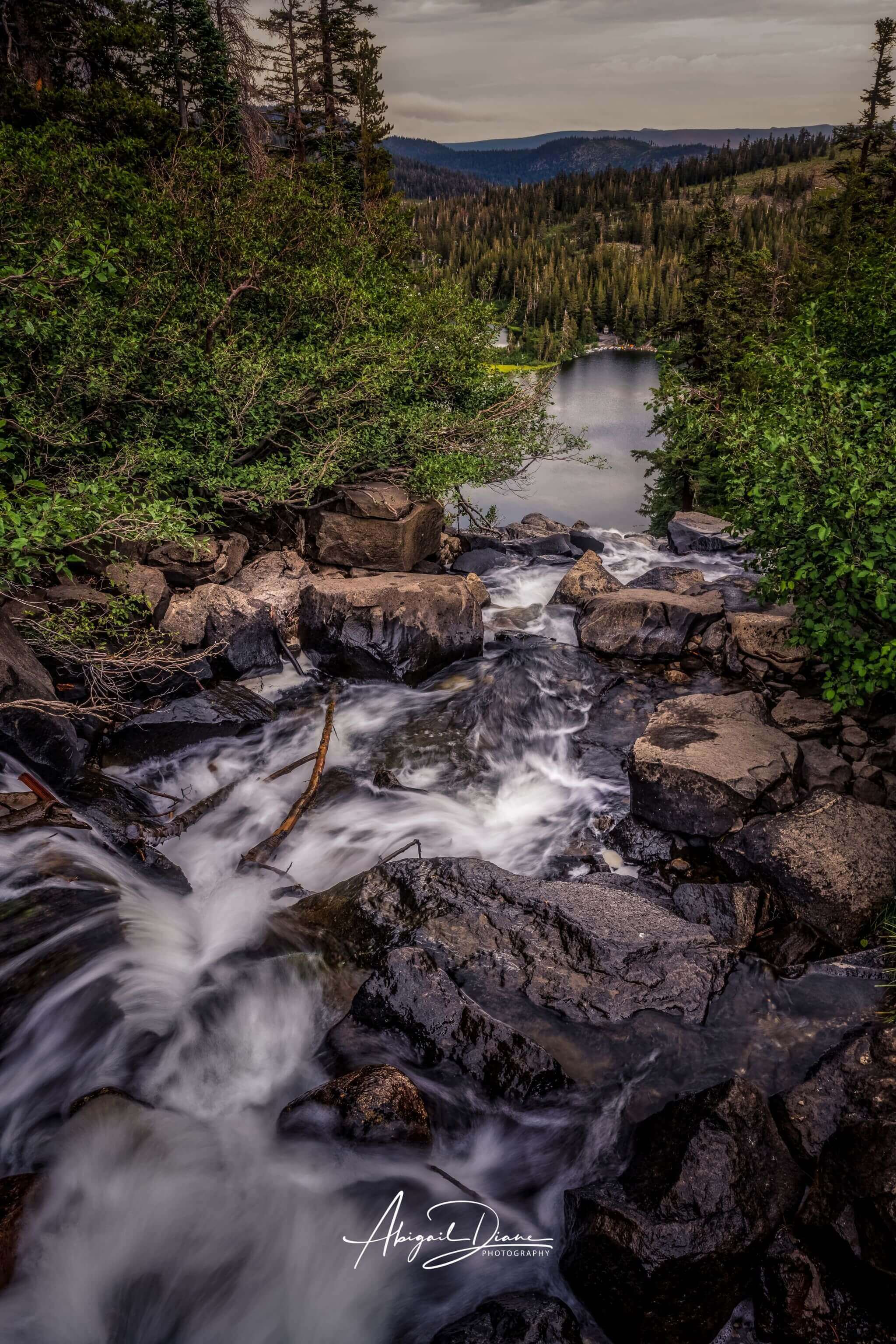 Cascading Into Stillness, long-exposure photograph of Twin Falls flowing over rugged rocks towards Twin Lake, in Mammoth Lakes, California. Photographed by Abigail Diane Photography.