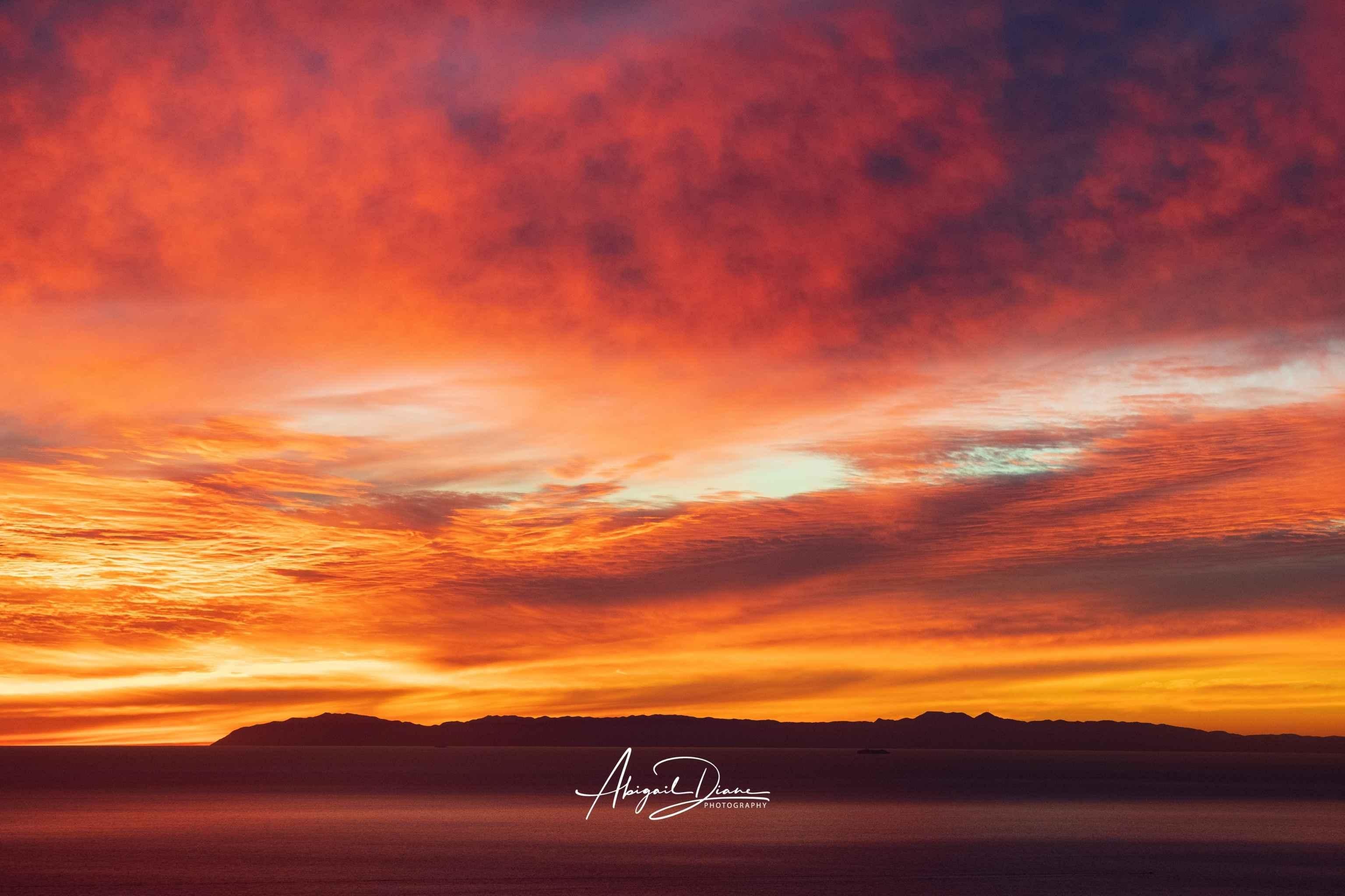 Catalina Beneath Crimson Skies fine art photography print featuring a dramatic Southern California sunset with crimson clouds, glowing orange skies, and the silhouette of Catalina Island over the Pacific Ocean.