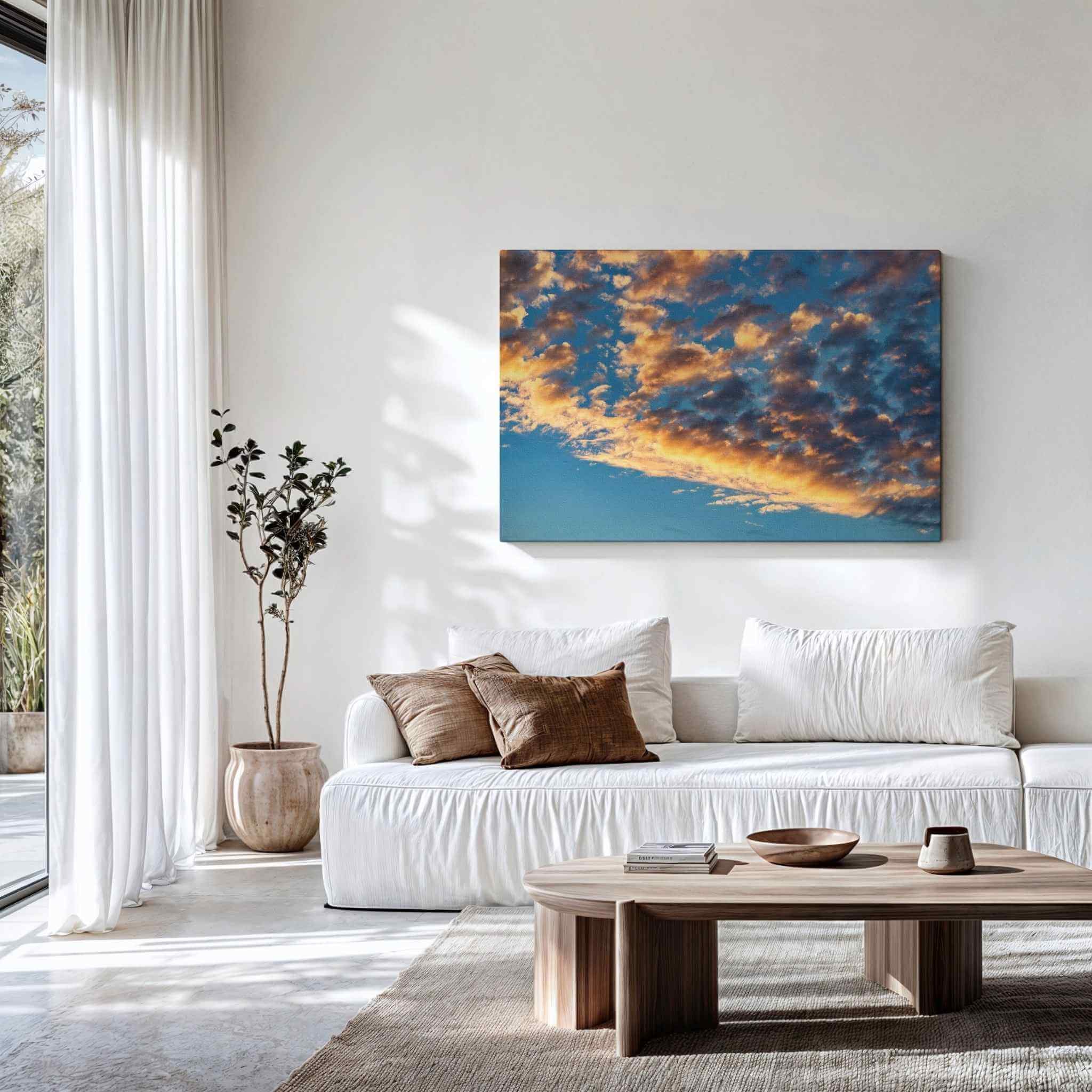 Gallery wrapped canvas of Gold and Blue Symphony of the Sky displayed above a contemporary white sofa, featuring dramatic golden clouds illuminated against a deep blue evening sky. Fine art cloudscape wall decor by Abigail Diane Photography.