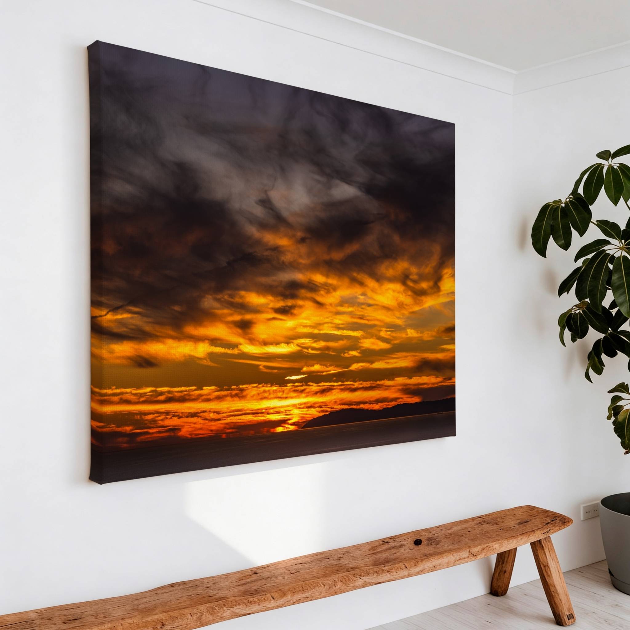Gallery wrapped canvas featuring a dramatic golden sunset displayed above a rustic wooden bench in a minimalist living room with a large indoor plant.