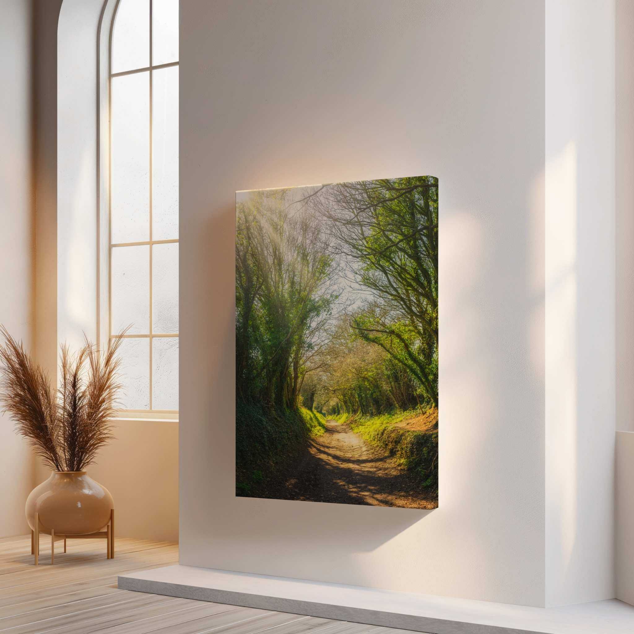 Wrapped canvas print of Halnaker Tree Tunnel by Abigail Diane Photography displayed in a bright modern interior with floor-to-ceiling arched windows and warm natural light. This peaceful woodland scene from West Sussex, England creates a calming focal point in contemporary home décor.