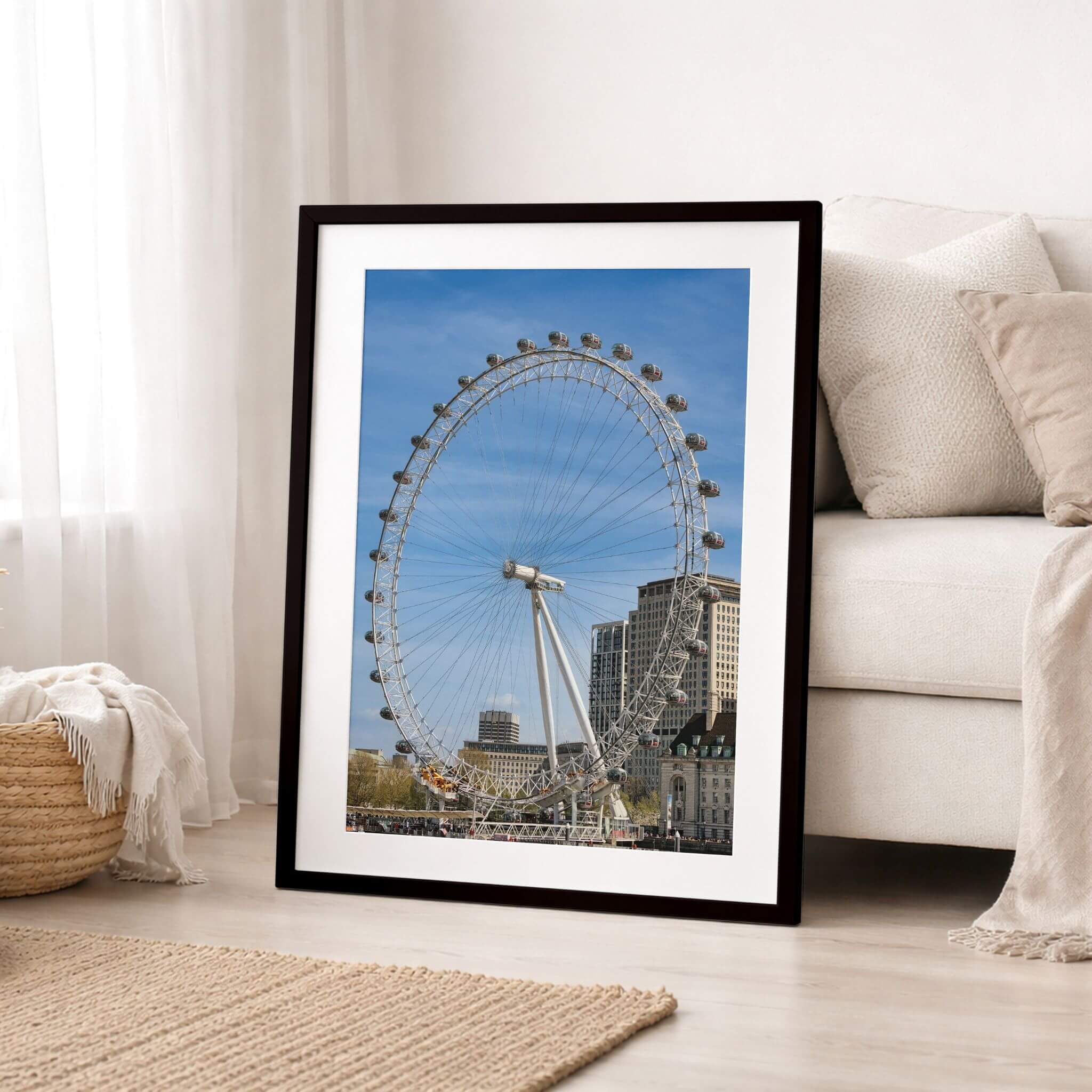 London Eye fine art print displayed in a black frame with white mat beside a neutral sofa in a bright contemporary living room.