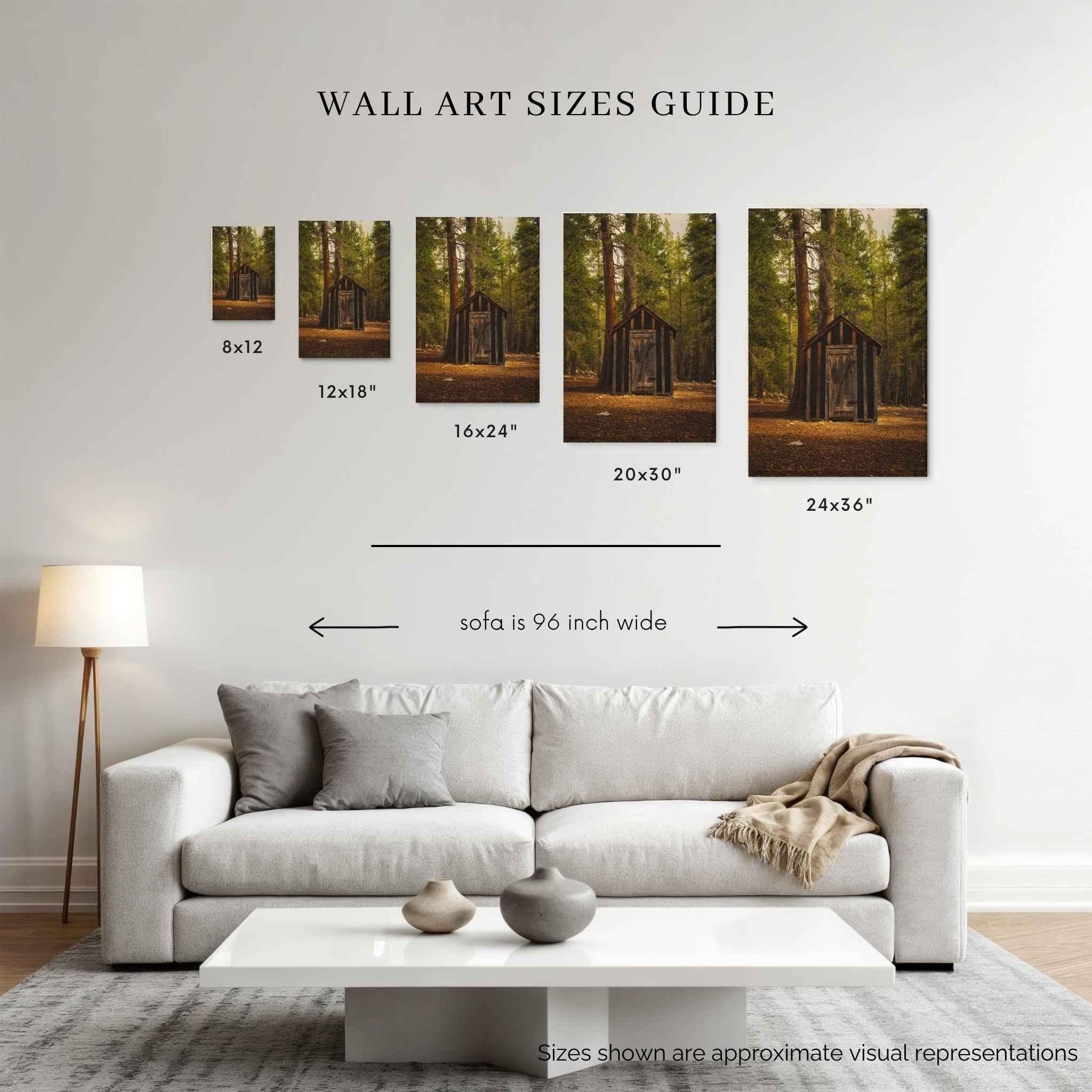 A wall art sizes guide displayed on a living room wall above a white sofa, showing five framed forest wall art prints of rustic remnant among the trees, with dimensions labeled 8x12, 12x18, 16x24, 20x30, and 24x36, plus a note that the sofa is 96 inch wide.