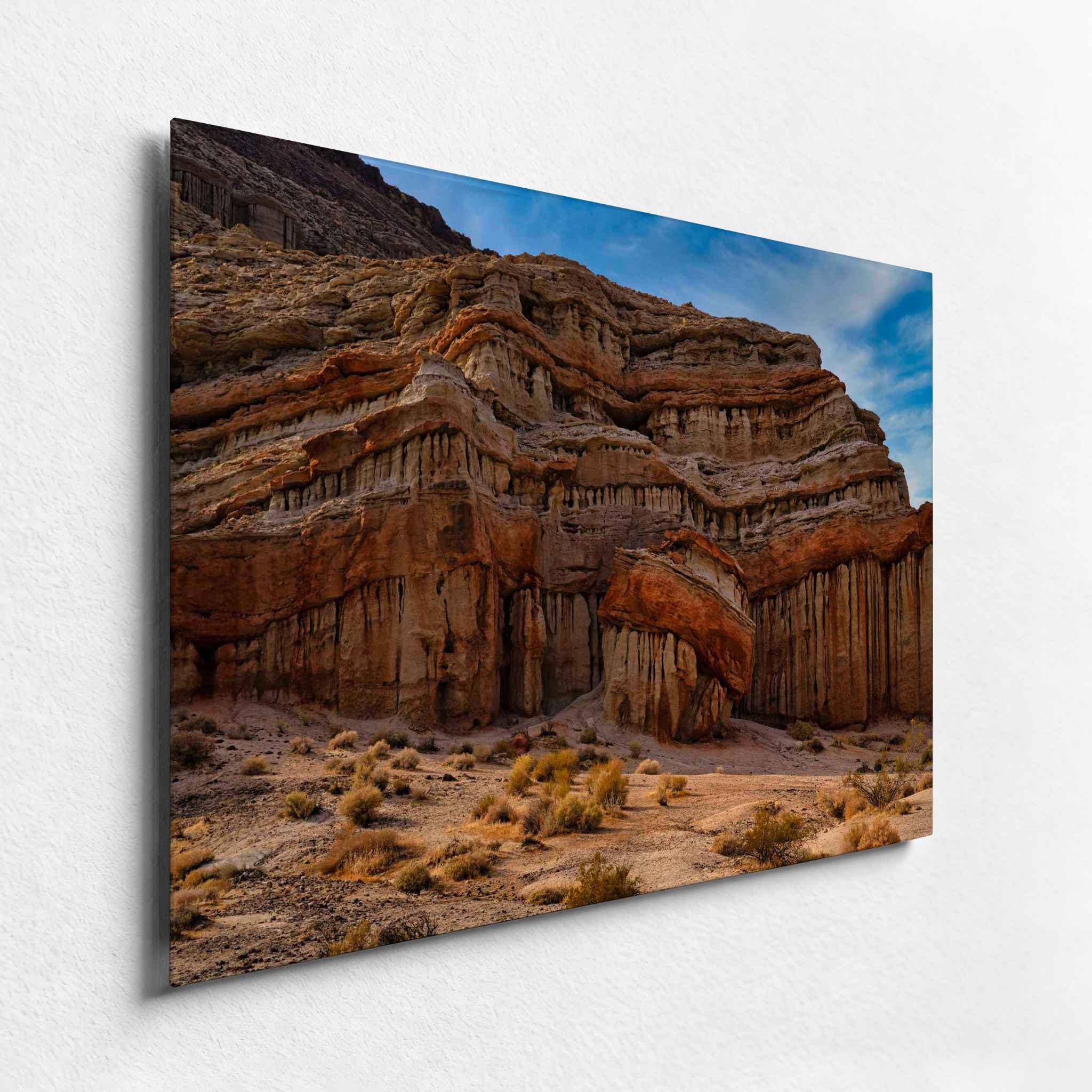 Sculpted California desert cliffs with layered red and ochre rock formations, shown as an HD metal print from an angled side view.