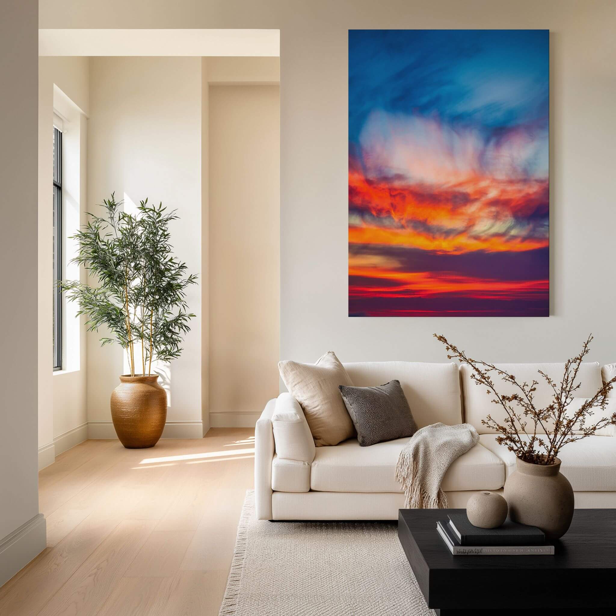 Smoldering Clouds high-definition metal print by Abigail Diane Photography displayed as large statement wall art above a cream sofa in a warm contemporary living room, featuring dramatic cobalt blue, crimson red, fiery orange, violet, and glowing golden clouds at sunset over the Pacific Ocean in Southern California.