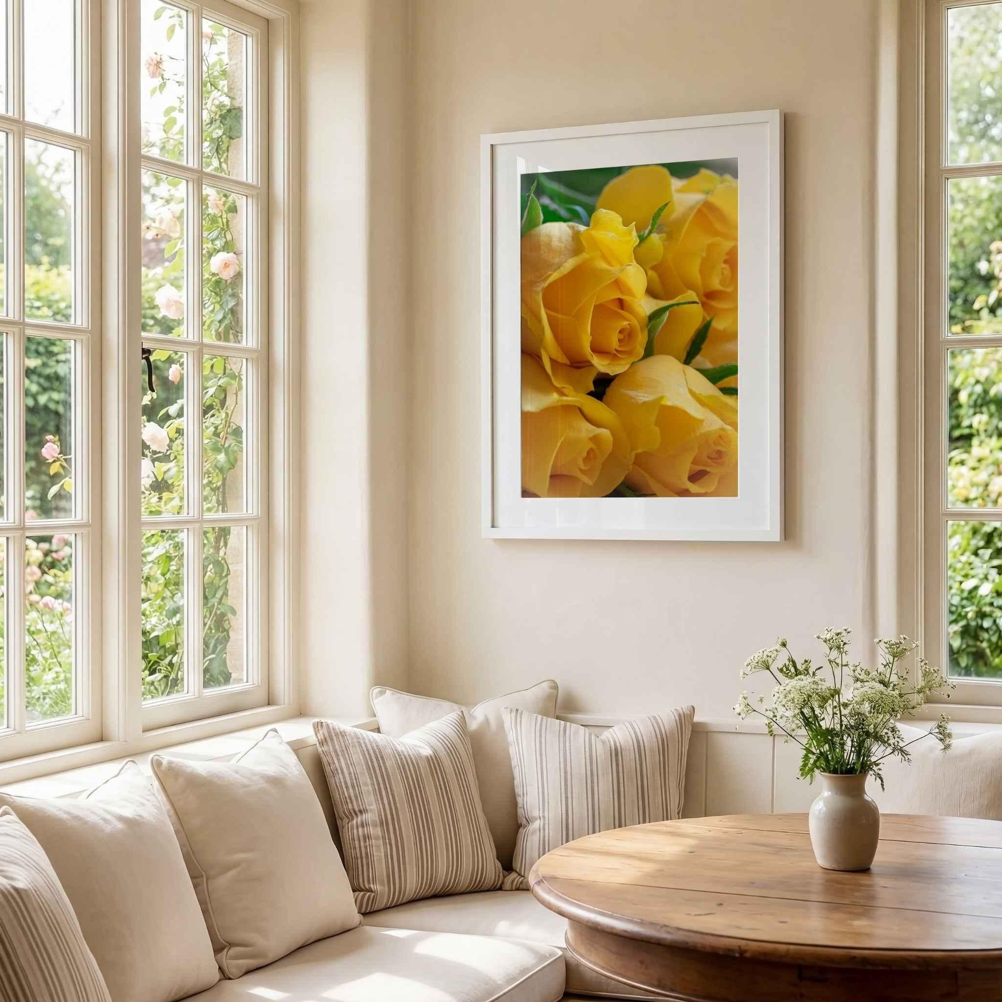 Sunlit Petal Reverie yellow rose photography by Abigail Diane Photography displayed in a white frame within a bright garden-inspired room featuring large windows, soft neutral furnishings, a wooden table, and blooming flowers outside.