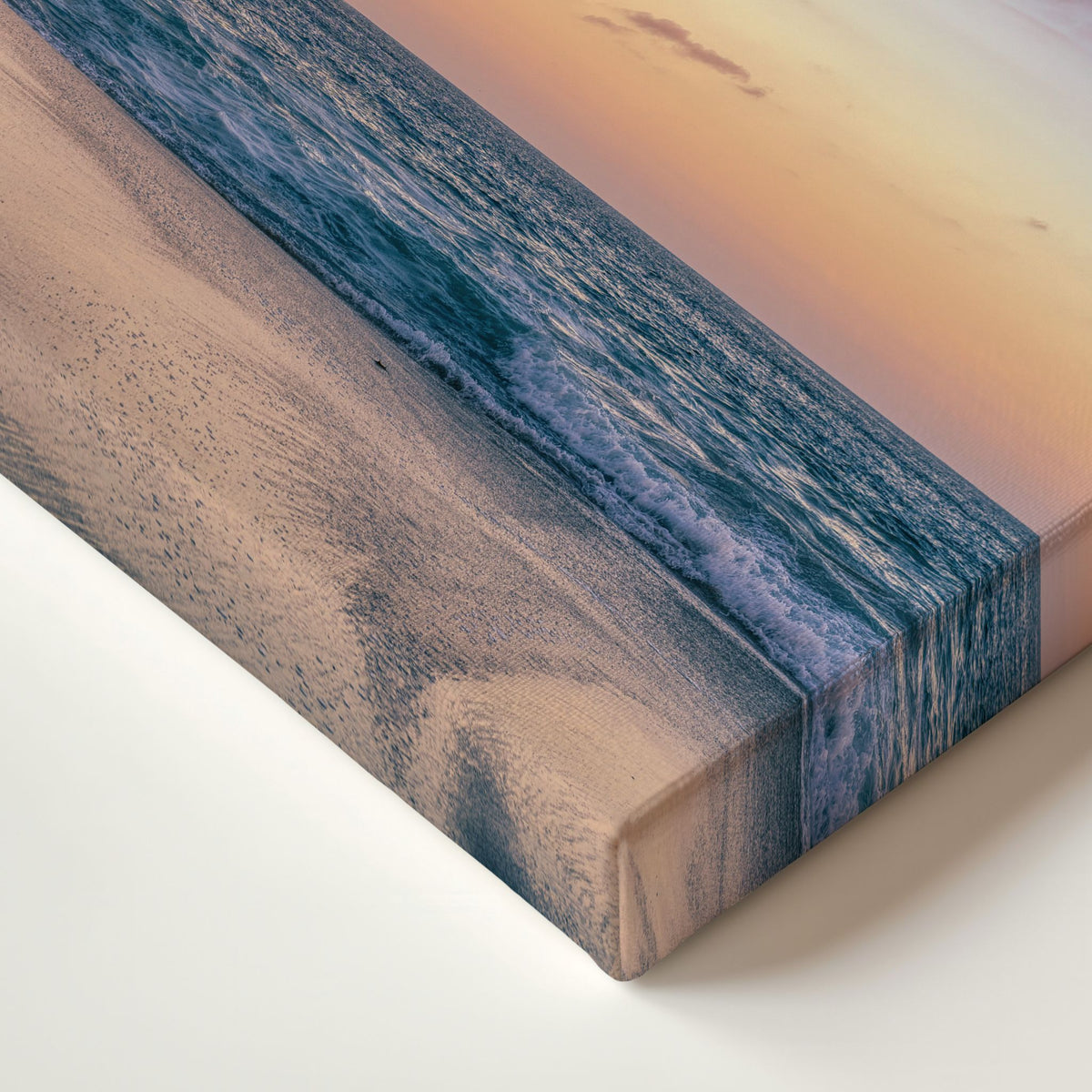crescent beach close-up of a rectangular canvas print showing a beach shoreline at sunset, with blue ocean waves, pale sand, and a warm peach sky.