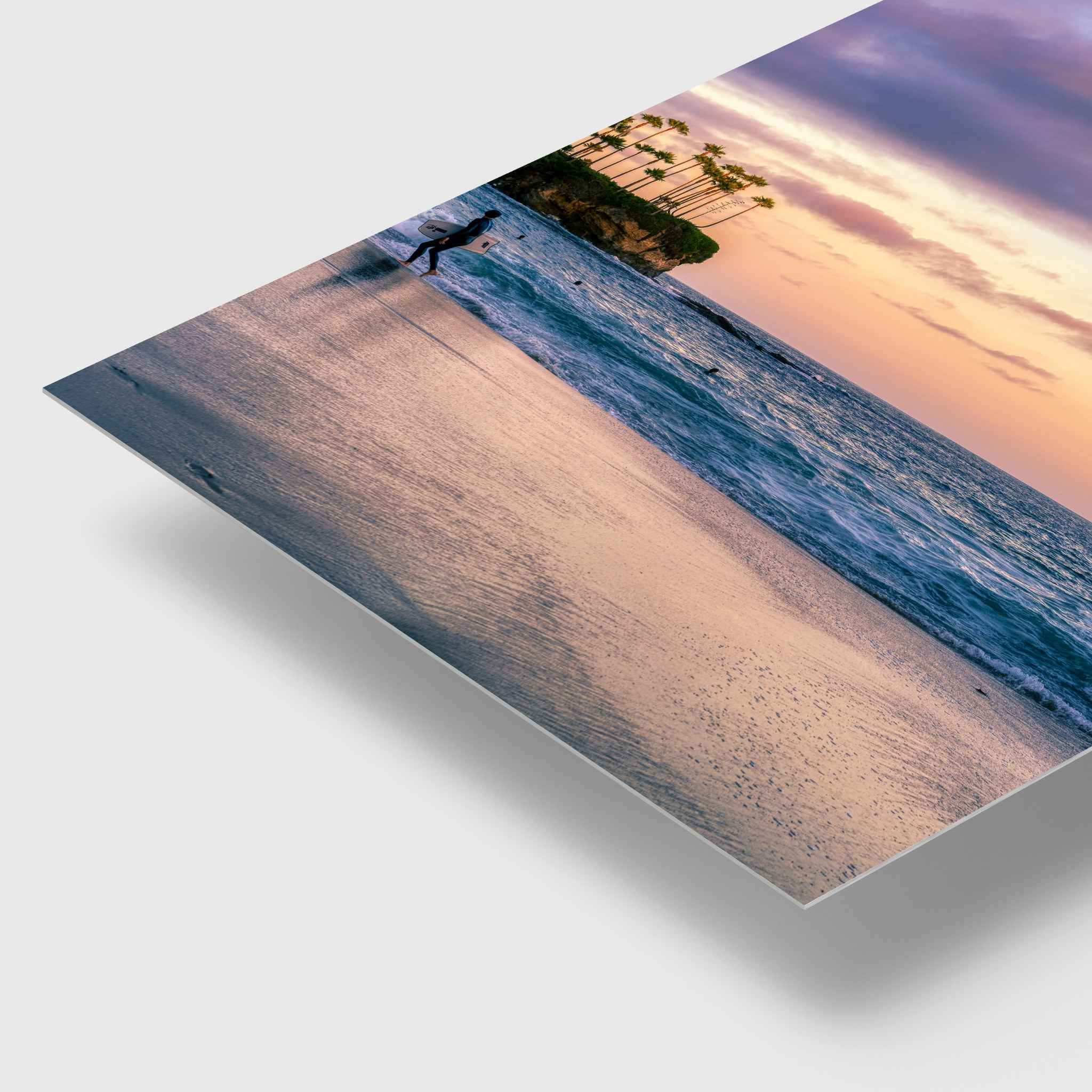 Surfing a California Sunset dye-sublimation metal print by Abigail Diane Photography featuring a vibrant Laguna Beach California sunset with a beach shoreline at sunset, photographed at an angle on a light gray background with a soft shadow underneath.