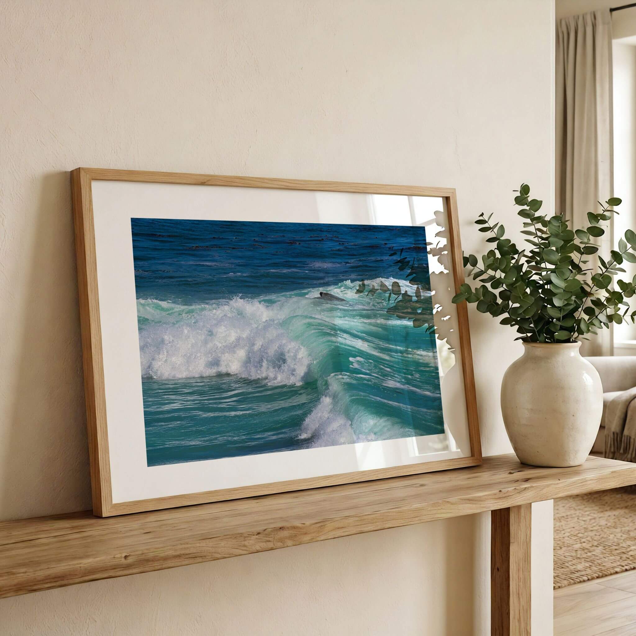 Framed Turquoise Healing Waves print displayed on a wooden console table beside greenery, featuring the vibrant turquoise waters of Laguna Beach on California's Pacific coastline. Fine art photography by Abigail Diane Photography.