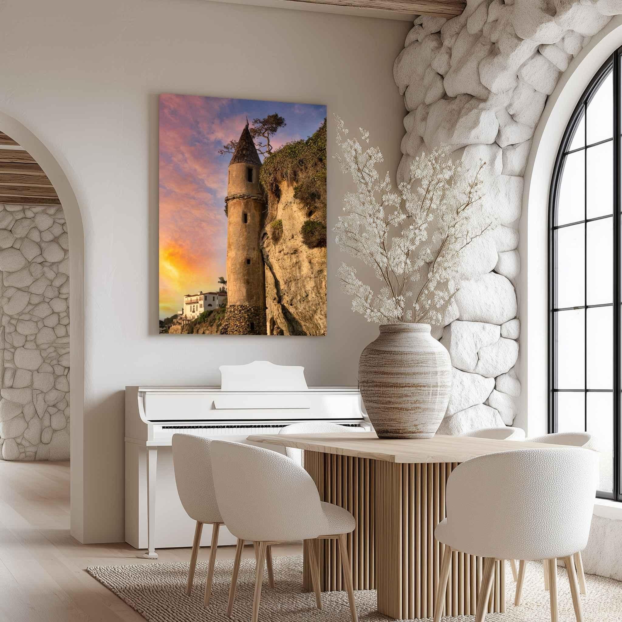 Large gallery wrapped canvas print of Victoria Beach Pirate Tower at sunset in Laguna Beach, California, displayed in an elegant dining room with natural stone walls, warm neutral furnishings, and abundant daylight.