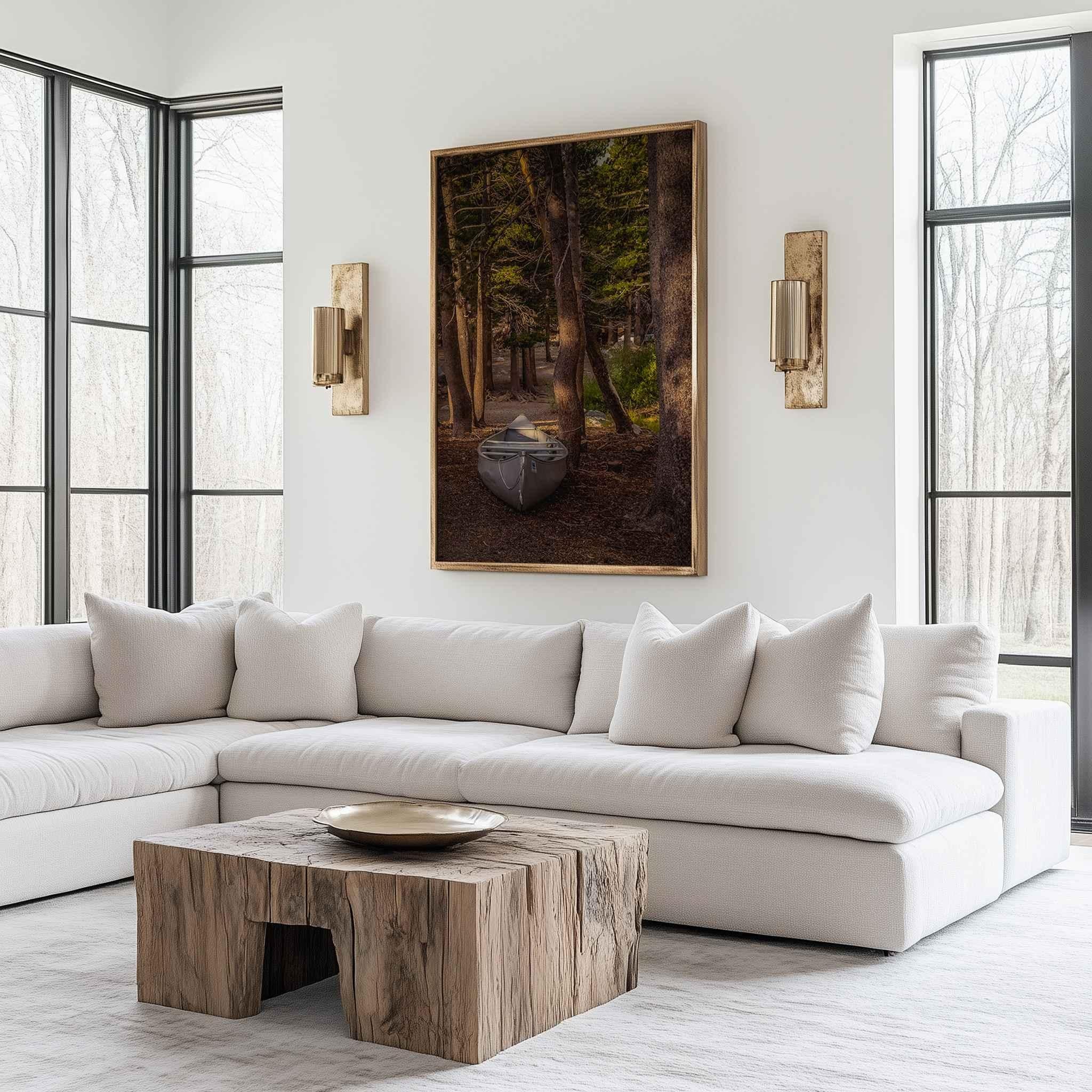 Waiting for the Water fine art print displayed in a natural wood frame above a white sofa, featuring a canoe resting among pine trees near Mammoth Lakes, California.