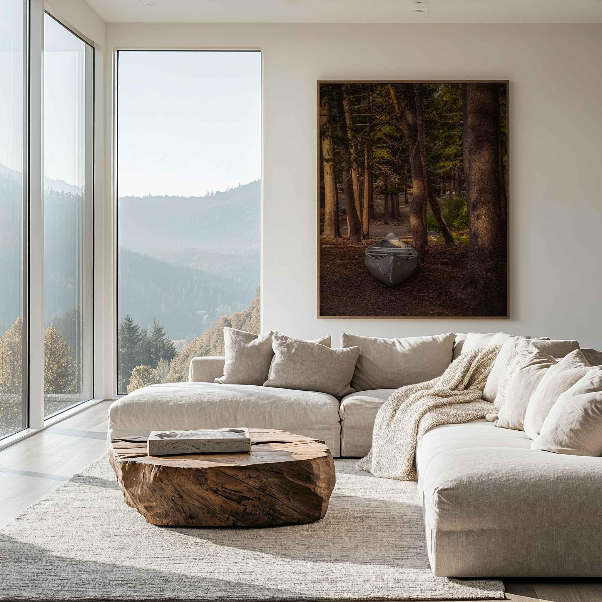 Waiting for the Water fine art print displayed in a natural wood frame above a white sofa in a modern living room, featuring a canoe among pine trees near Mammoth Lakes, California.