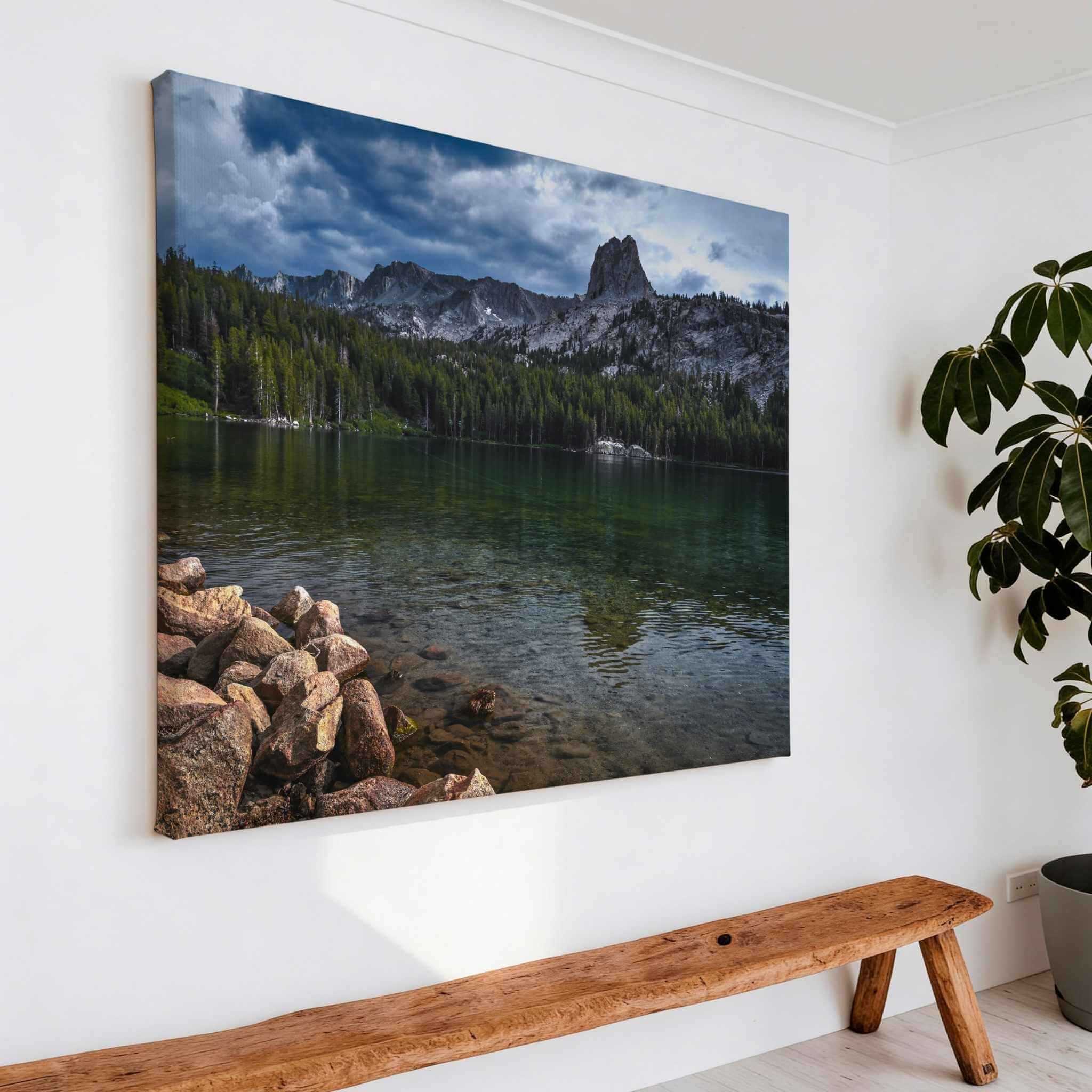 Large gallery-wrapped canvas featuring Where Mountains Meet Stillness, showcasing a peaceful mountain lake with granite peaks and pine forests in Mammoth Lakes, California, displayed above a handcrafted wooden bench in a bright modern entryway with natural décor by Abigail Diane Photography.