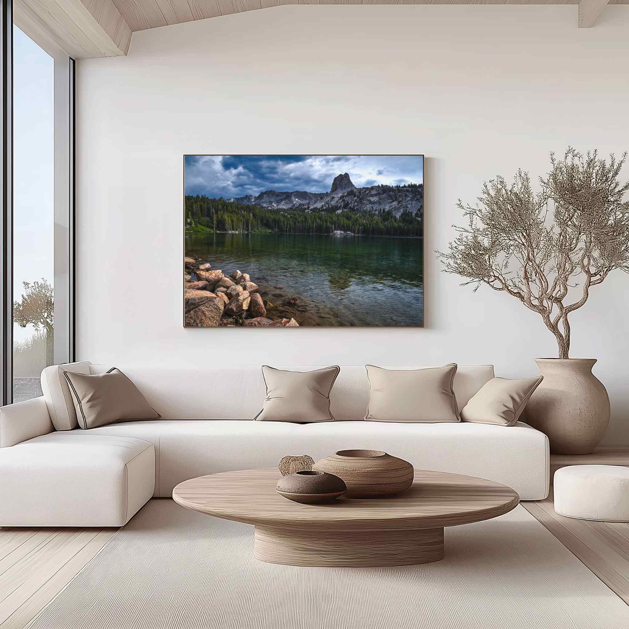 Large gallery-wrapped canvas featuring Where Mountains Meet Stillness, showcasing a serene mountain lake with granite peaks and pine forests in Mammoth Lakes, California, displayed above a cream sectional sofa in a bright contemporary living room with natural wood accents by Abigail Diane Photography.