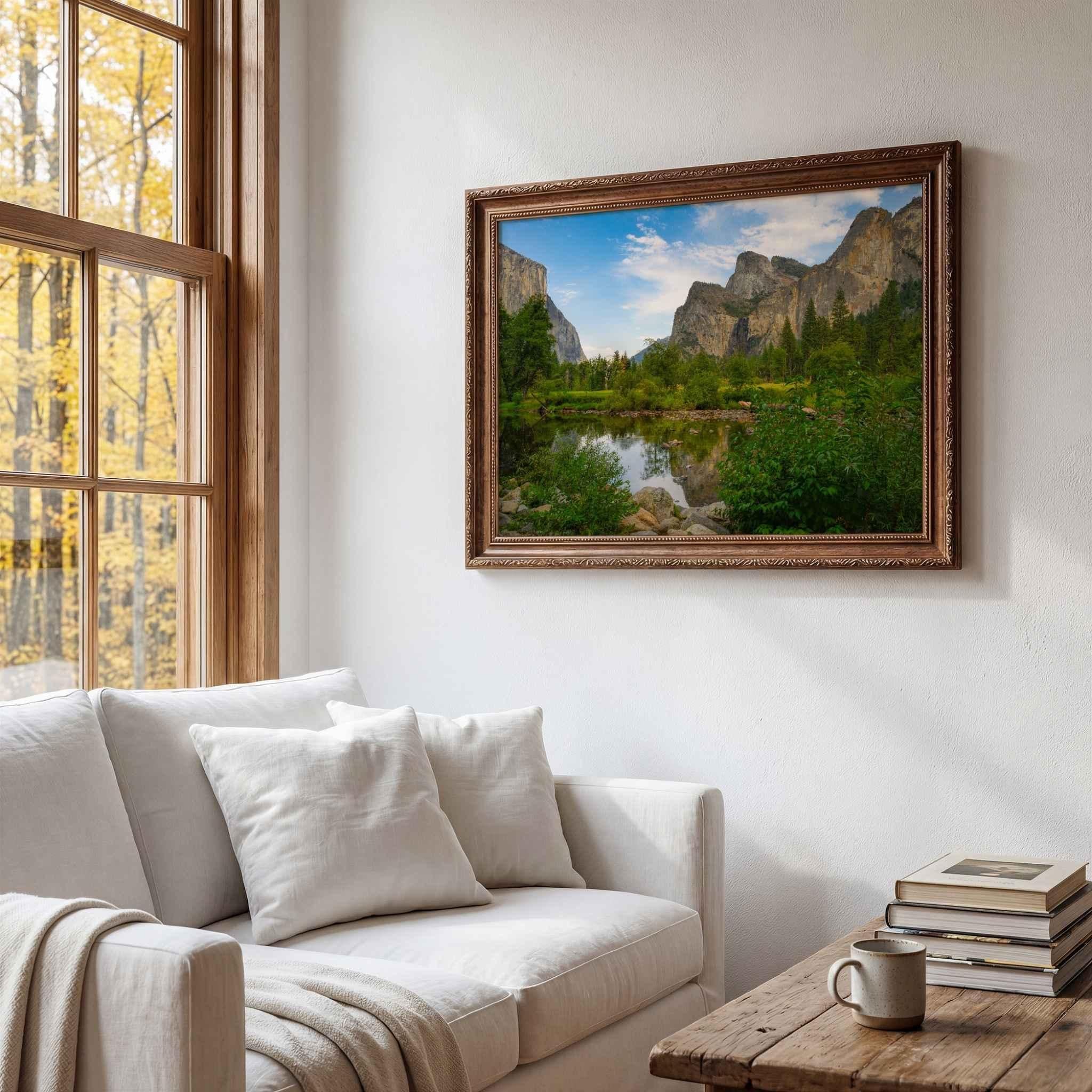 Yosemite Valley framed wall art by Abigail Diane Photography displayed above a white sofa in a cozy living room with a rustic wood coffee table, large windows overlooking autumn trees, and warm natural light.