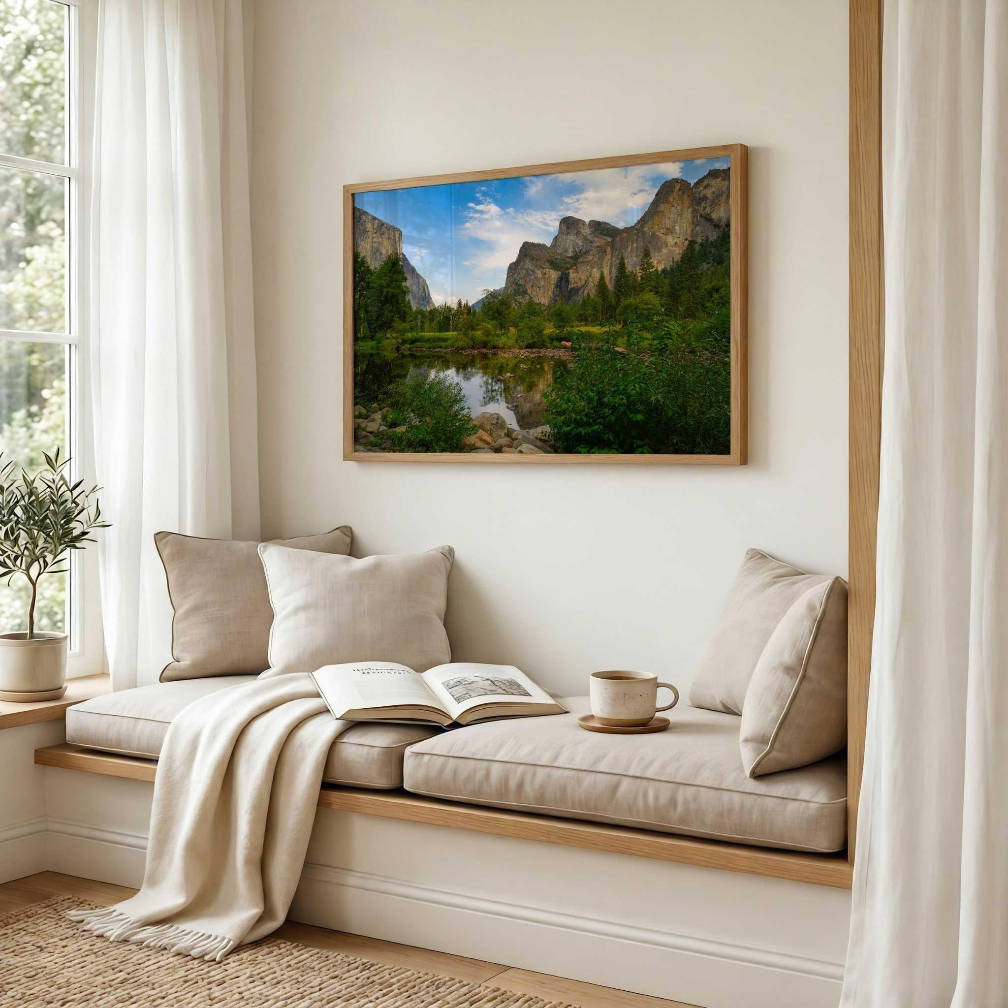 Oak-framed Yosemite Valley fine art print by Abigail Diane Photography displayed above a cozy window seat with cream cushions, a soft throw blanket, an open book, and warm natural light in a peaceful reading nook.