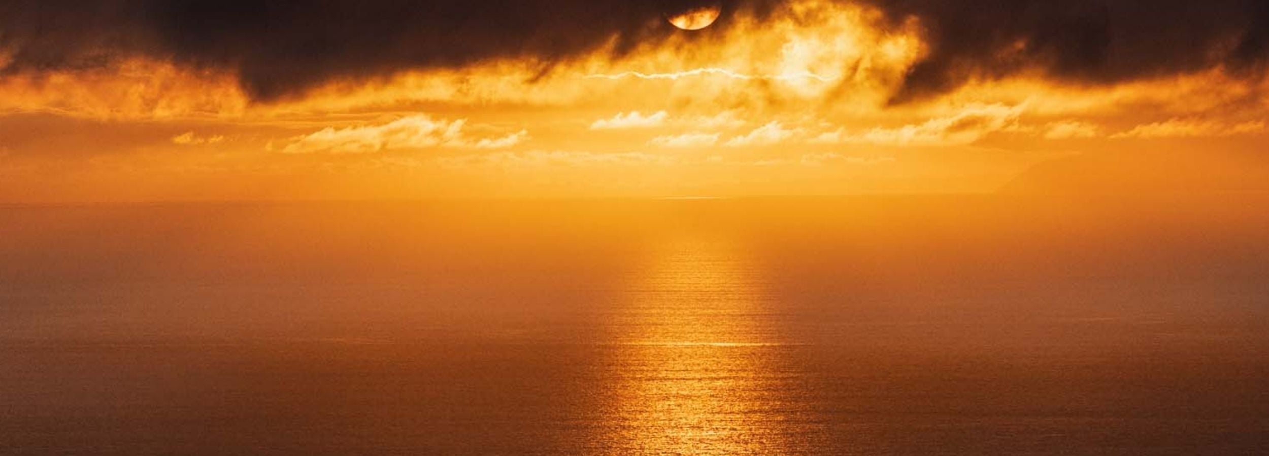 Golden Rays on the Mirrored Sea of the Pacific by Abigail Diane Photography featuring a dramatic golden sunset over the calm Pacific Ocean, with radiant sun rays reflecting across the water beneath moody clouds during golden hour.