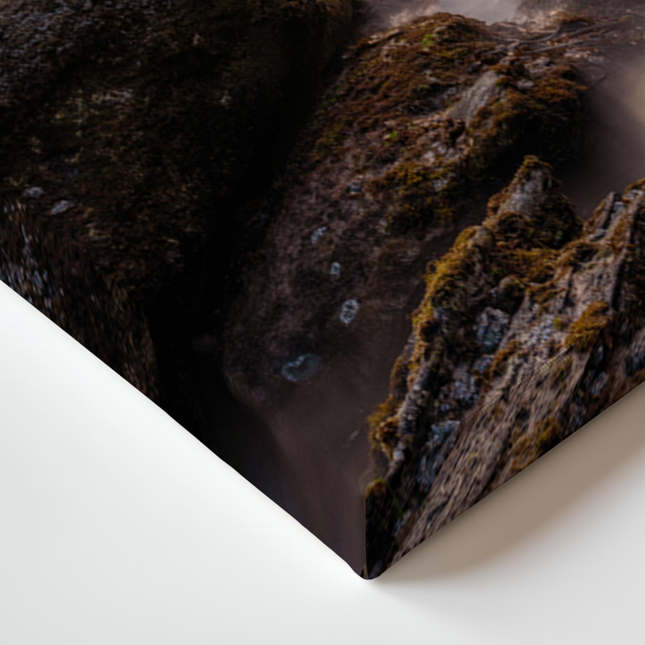 A close-up of a rectangular wall art print or canvas showing a dark rocky landscape with mossy textures, photographed against a clean white background.