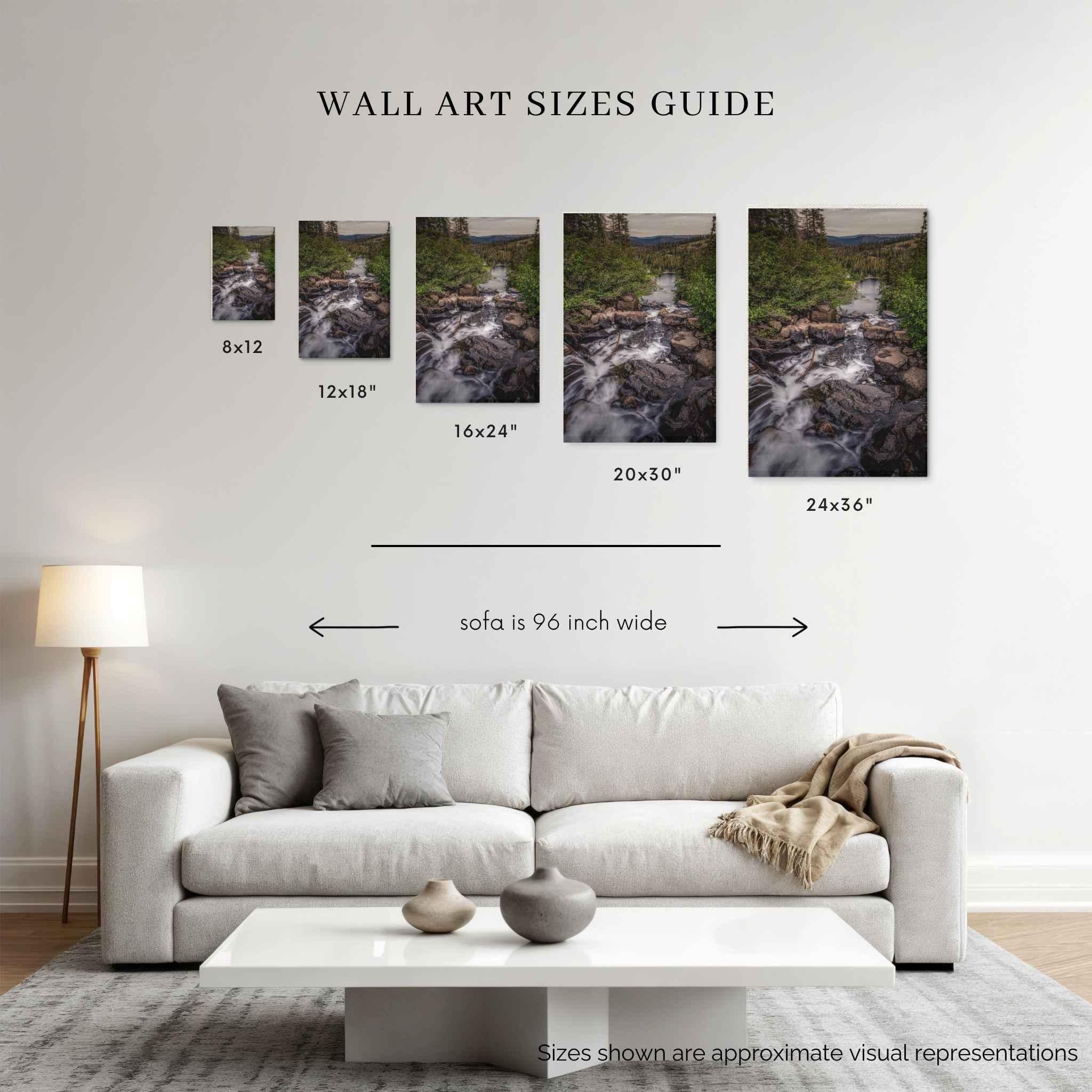 A wall art sizes guide displayed above a modern white sofa in a living room. The graphic shows five framed landscape prints of cascading into the stillness with dimensions labeled 8x12, 12x18, 16x24, 20x30, and 24x36, plus text noting the sofa is 96 inch wide.