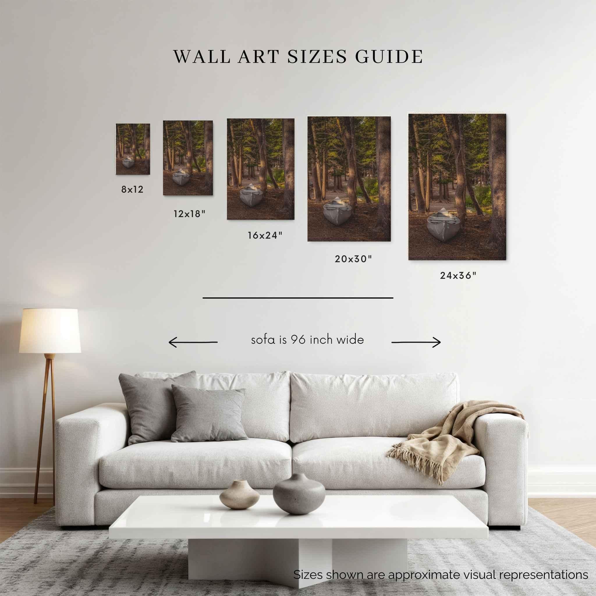 A wall art sizes guide mockup showing five framed forest fine art printed titled waiting for the water,  above a white sofa, with dimensions labeled 8x12, 12x18, 16x24, 20x30, and 24x36. 