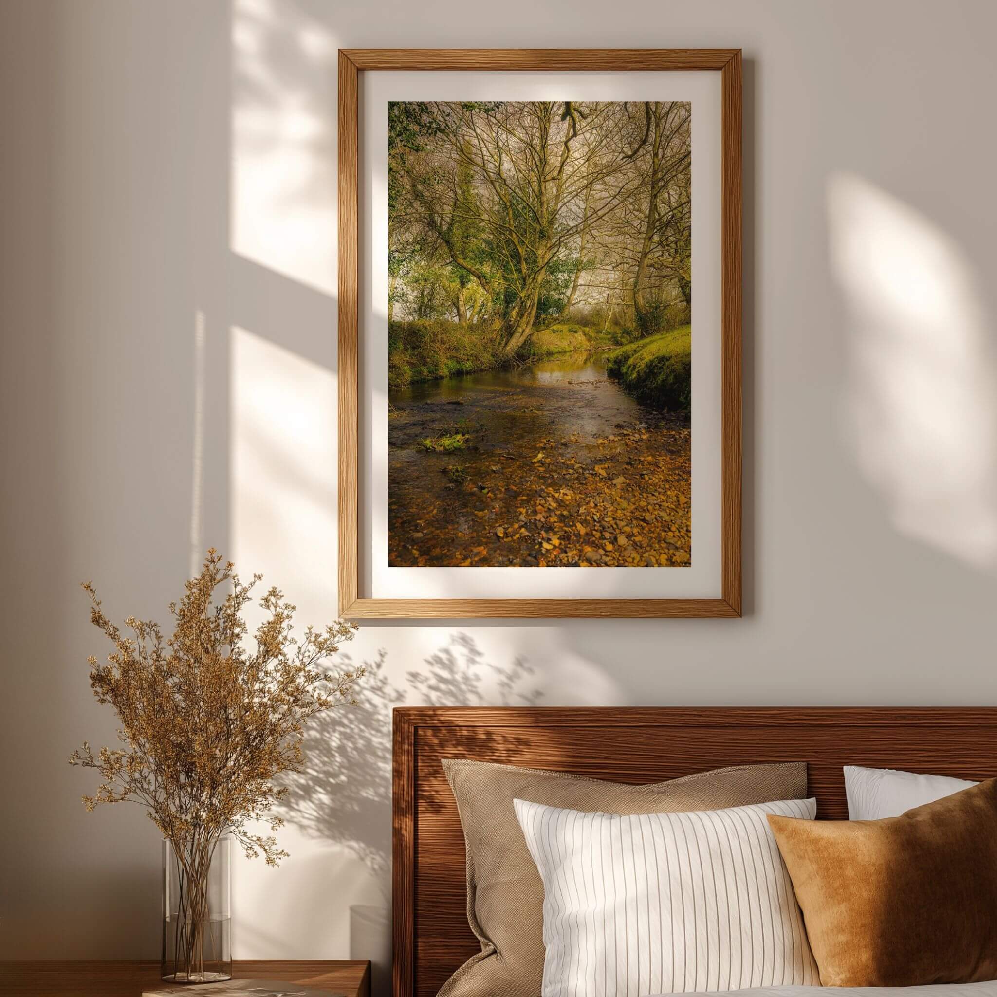 A Lazy Creek in the New Forest fine art print displayed above a wood bed in a warm neutral bedroom with soft natural light.