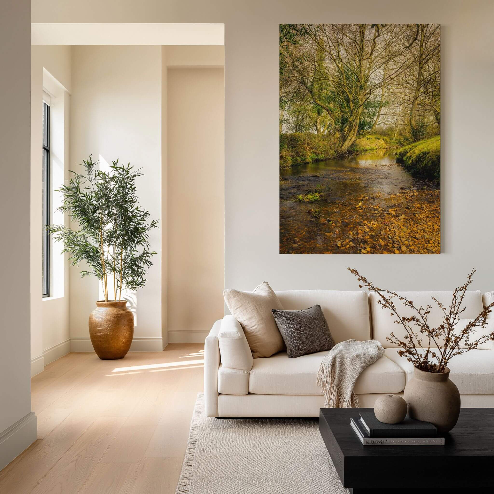 A Lazy Creek in the New Forest metal print displayed above a cream sofa in a warm neutral living room, featuring a peaceful woodland stream in the New Forest, England.