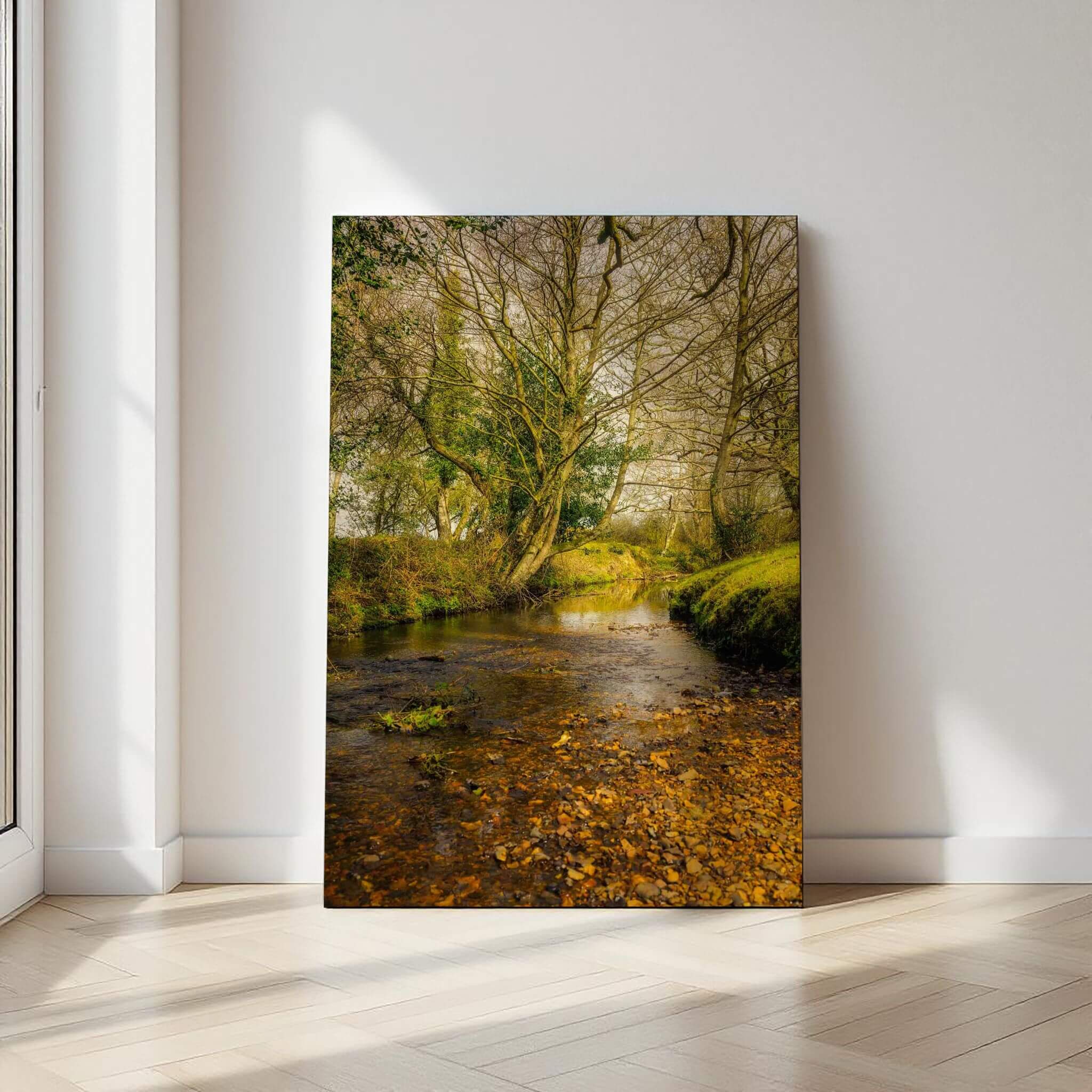 A Lazy Creek in the New Forest print displayed against a softly lit neutral wall, featuring a peaceful woodland stream.