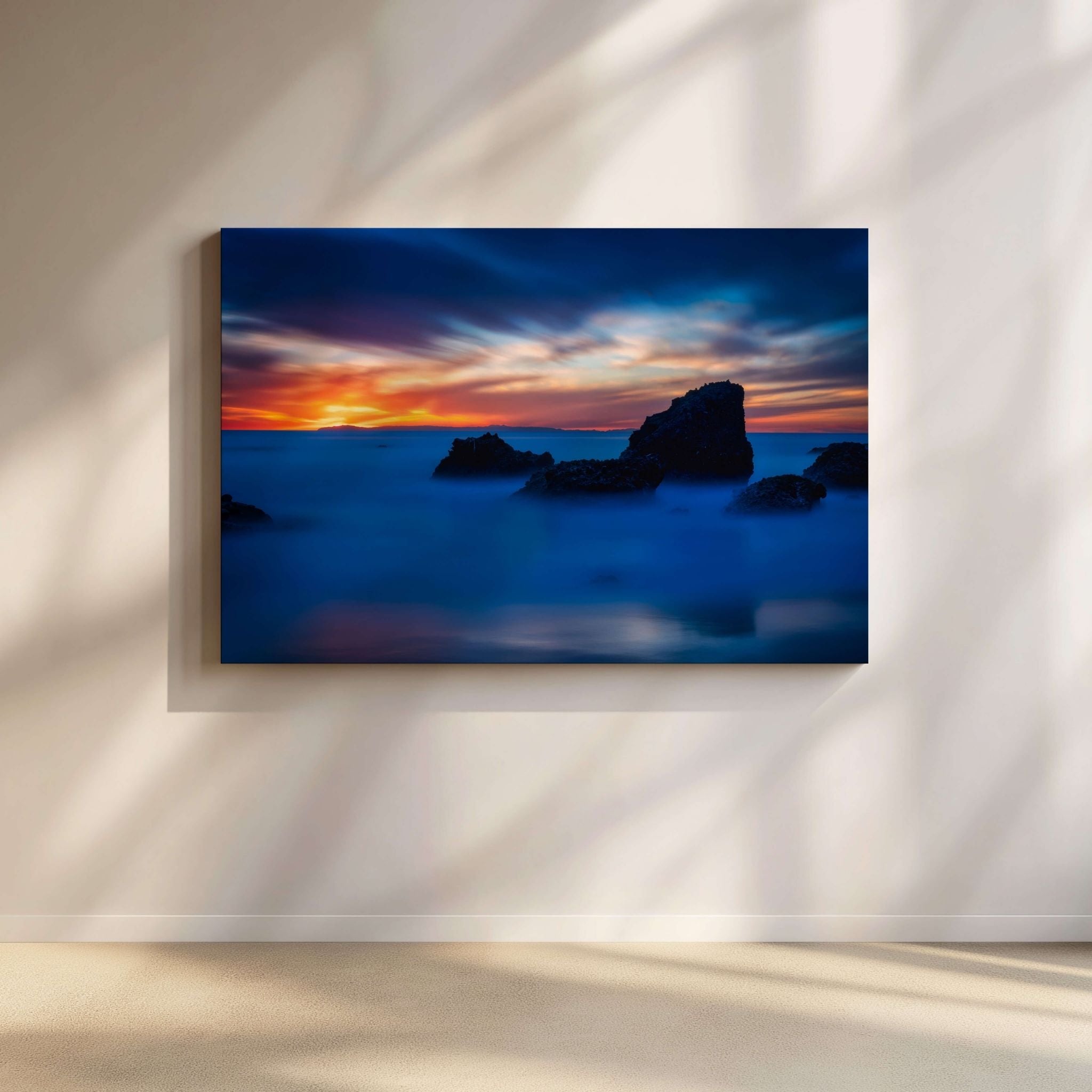 A Mystical Blue Hour gallery-wrapped canvas by Abigail Diane Photography displayed in a contemporary minimalist living room. This fine art photograph captures the tranquil blue hour at Woods Cove, Laguna Beach, California, where silky ocean waters surround dramatic sea stacks beneath a vibrant sunset sky of deep blue, orange, and violet, creating a peaceful coastal atmosphere perfect for modern interiors.