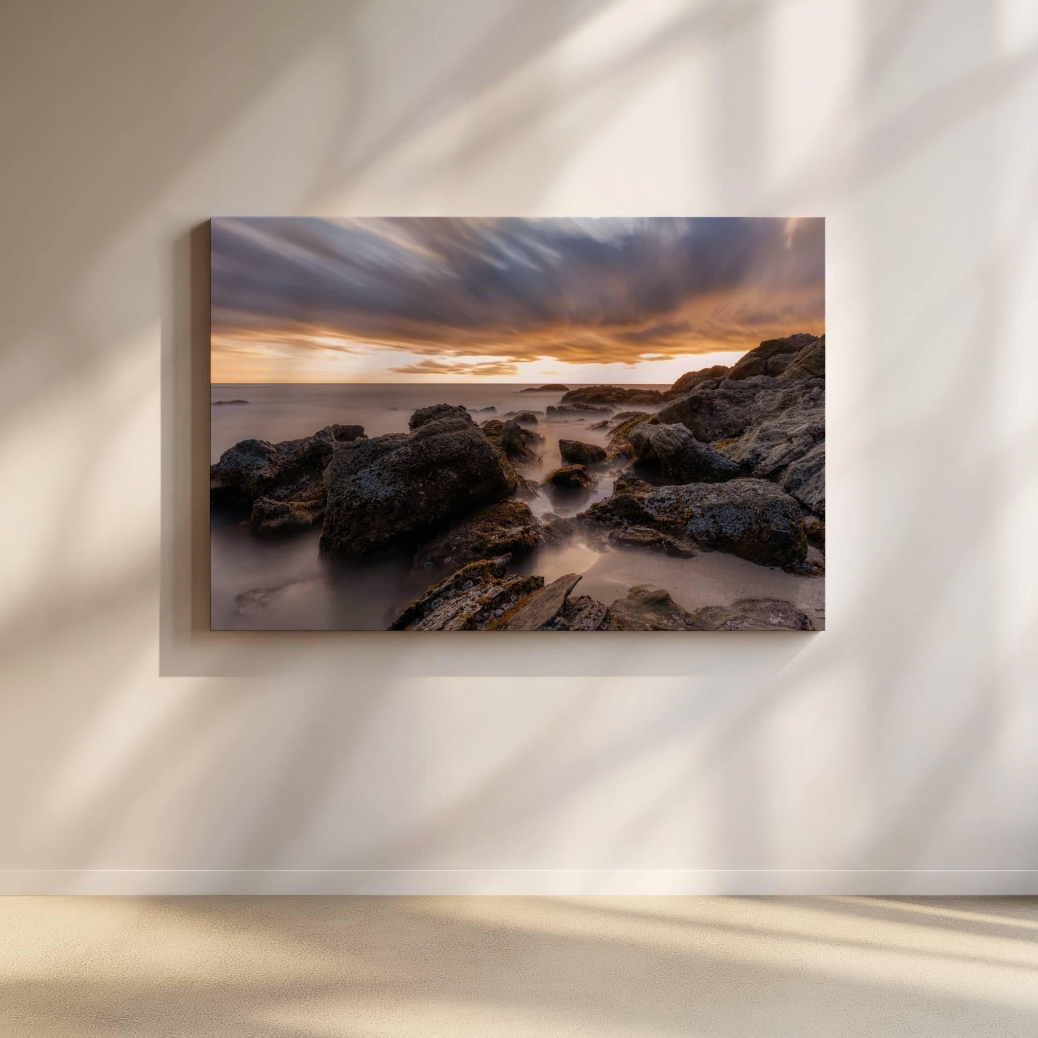 Large canvas print of After the Storm displayed on a warm neutral gallery wall, featuring a long exposure sunset over the rocky shoreline of Laguna Beach, California.