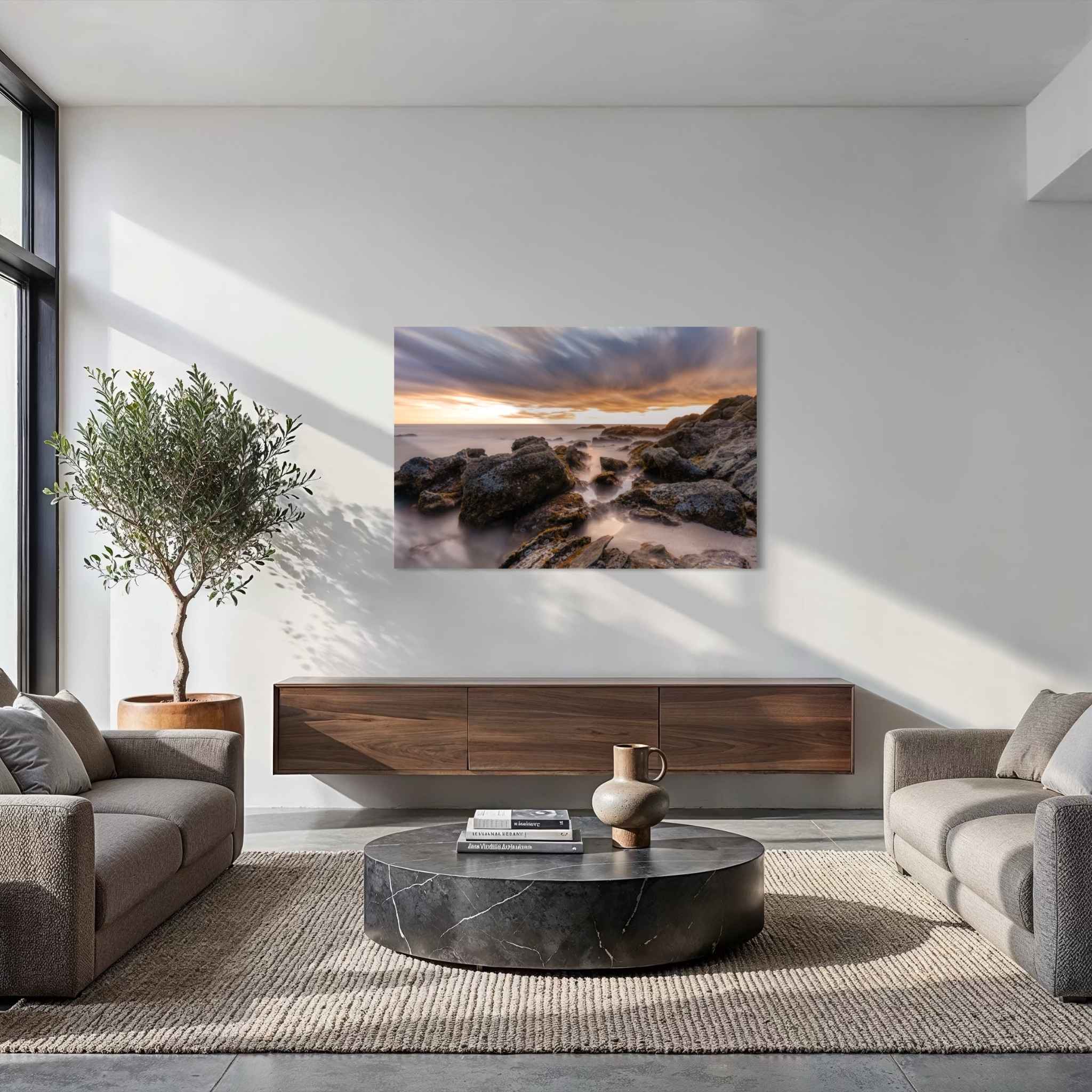 After the Storm dye-sublimation metal print by Abigail Diane Photography displayed in a contemporary living room with neutral furnishings, featuring a long-exposure sunset over rugged coastal rocks at Laguna Beach, California.