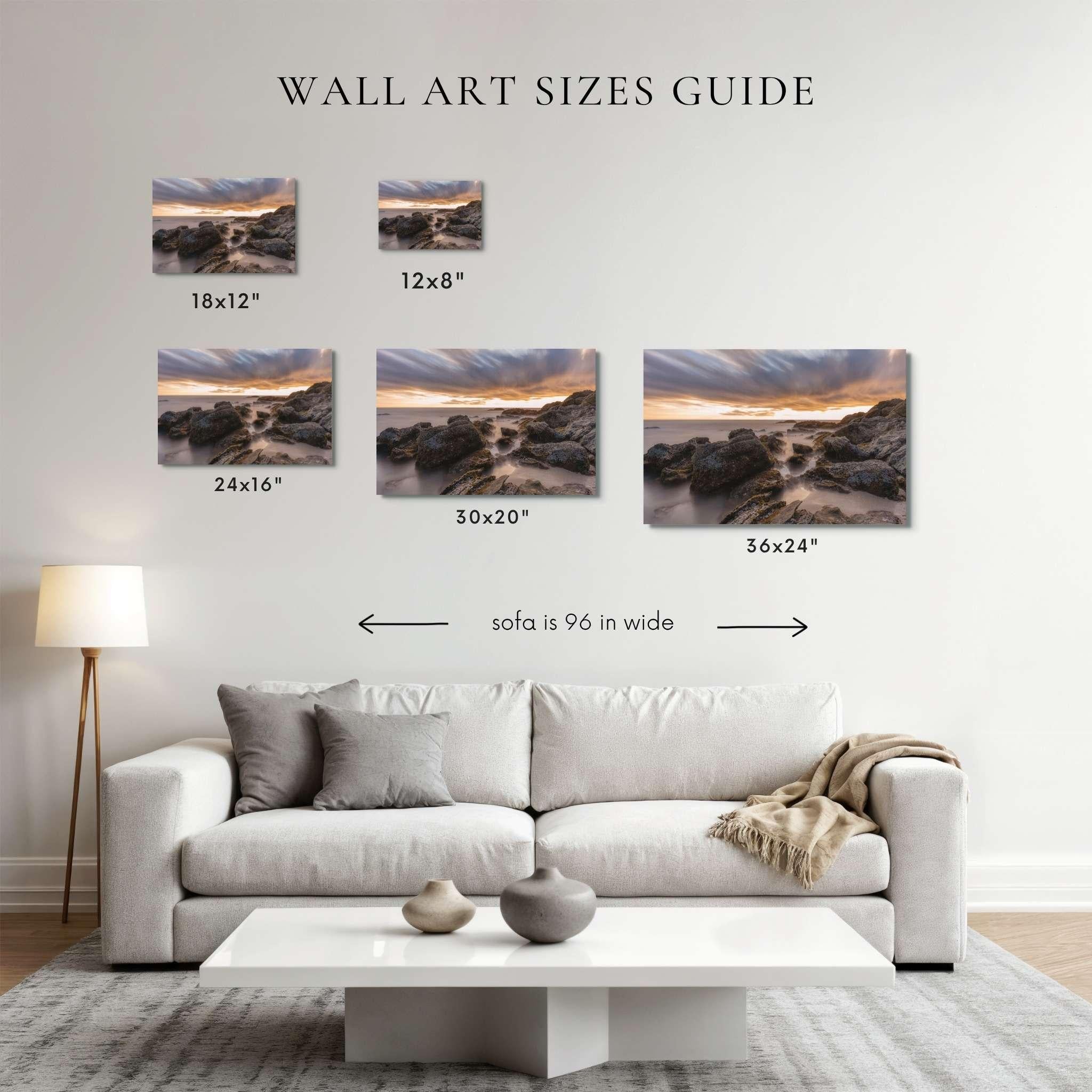 A wall art sizes guide mockup showing five coastal landscape canvas prints above a light gray sofa in a living room. The prints are labeled 18x12", 12x8", 24x16", 30x20", and 36x24", with text indicating sofa width is 96 in.