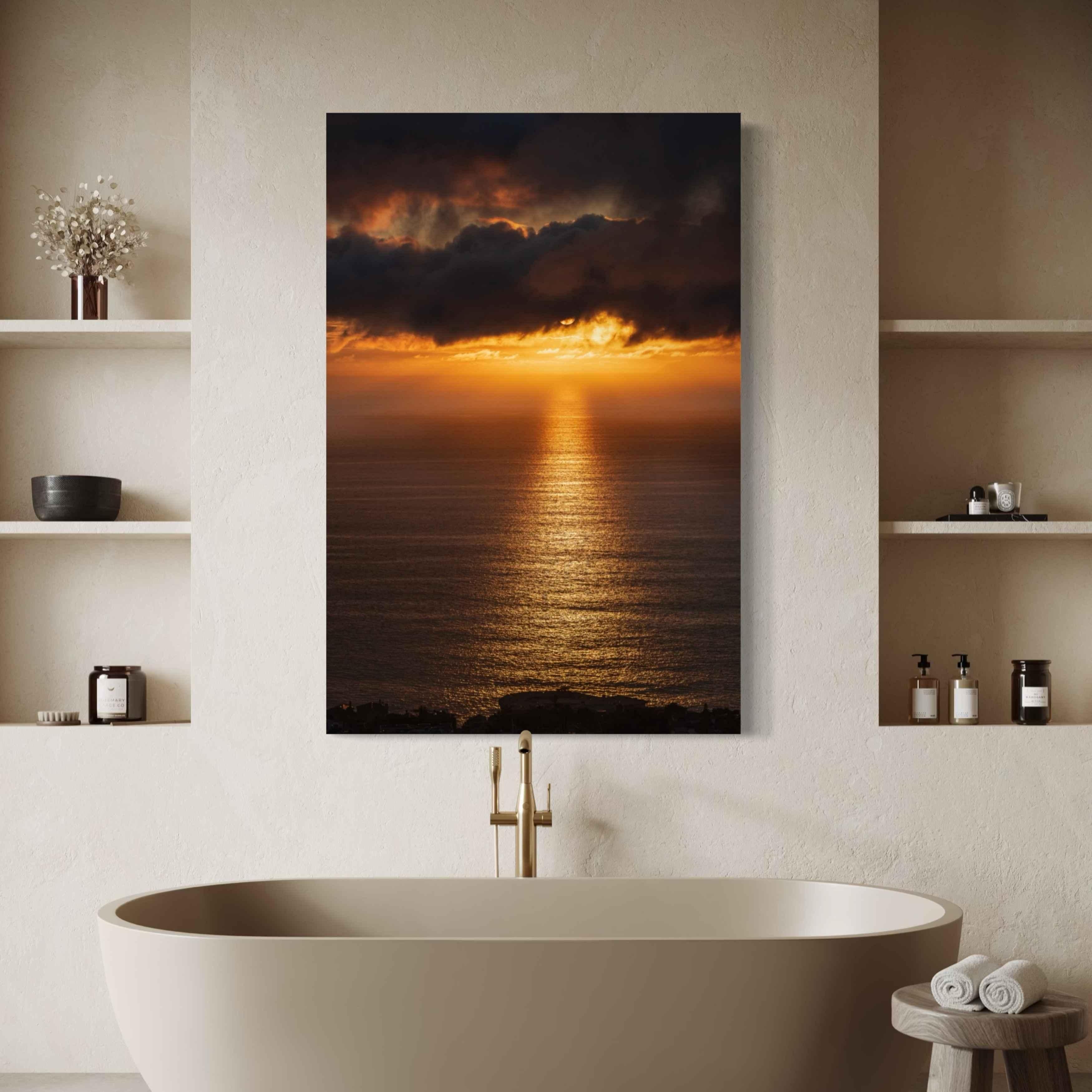 Luxury spa-inspired bathroom featuring Abigail Diane Photography's Laguna Beach Winter Sunset wrapped canvas print displayed above a freestanding soaking tub with brushed brass fixtures. Warm golden reflections across the Pacific Ocean and dramatic winter storm clouds create a calming focal point, complemented by minimalist built-in shelving, soft neutral textures, natural stone finishes, and modern coastal décor for a serene wellness retreat.