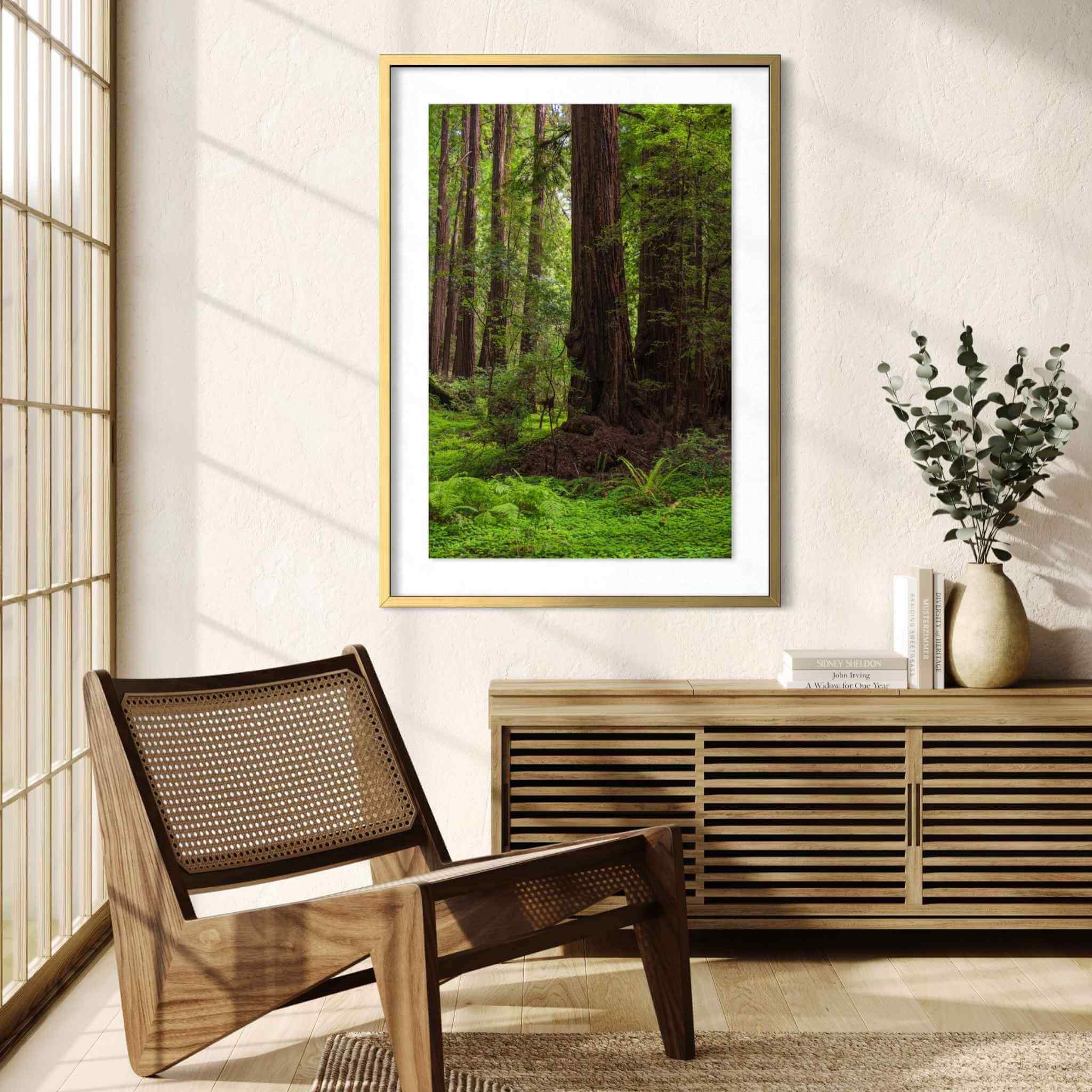 Ancient Stillness Among the Redwoods framed California redwood forest wall art by Abigail Diane Photography displayed in a warm Scandinavian-inspired living room with a natural oak and cane lounge chair, slatted oak console, ceramic vase with eucalyptus, textured rug, and floor-to-ceiling windows filling the space with soft natural light and a peaceful, nature-inspired atmosphere