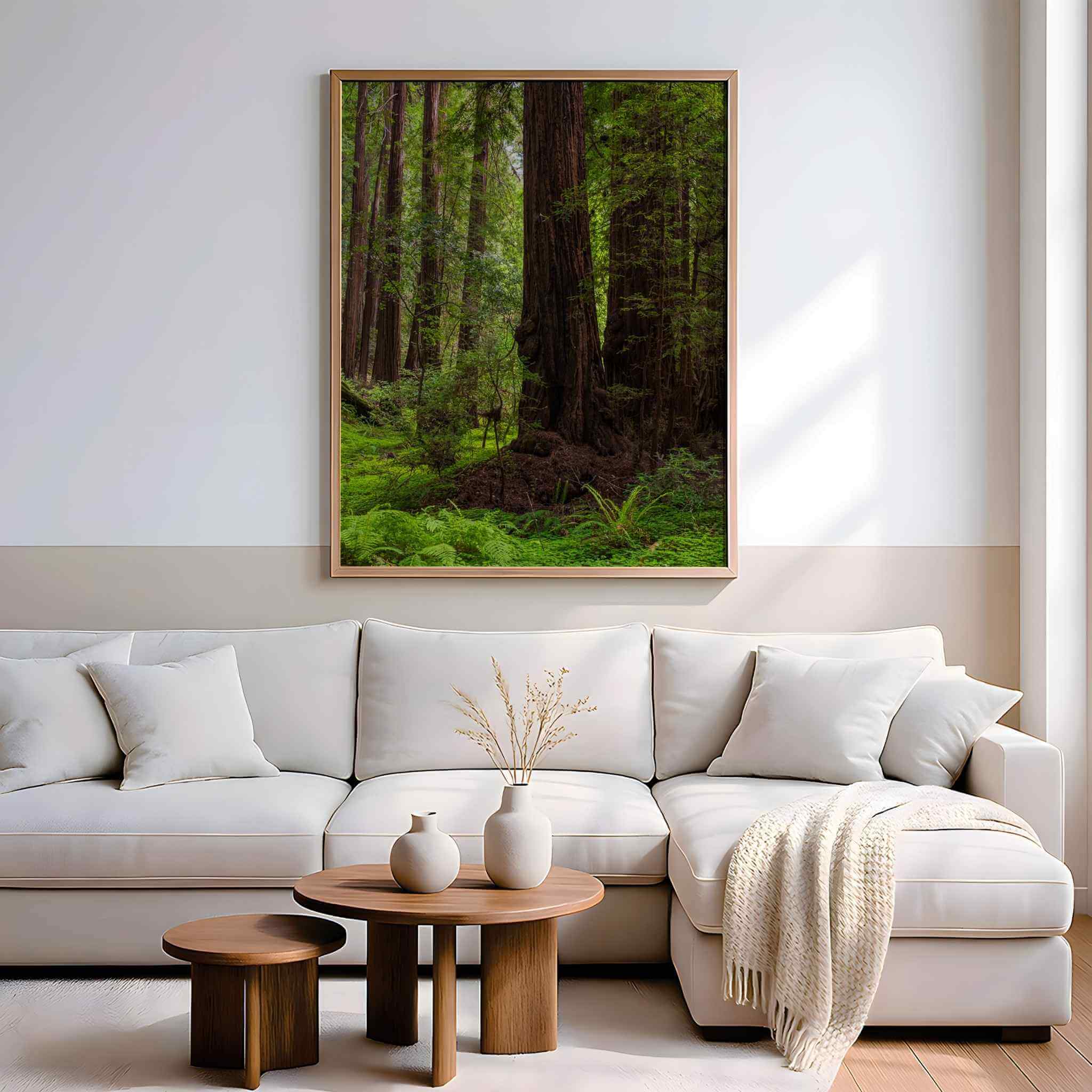 Ancient Stillness Among the Redwoods framed California redwood forest wall art by Abigail Diane Photography displayed above a cream sectional sofa in a modern living room with warm wood nesting tables, soft neutral décor, textured throw blanket, ceramic vases, and natural sunlight creating a calm, nature-inspired interior.