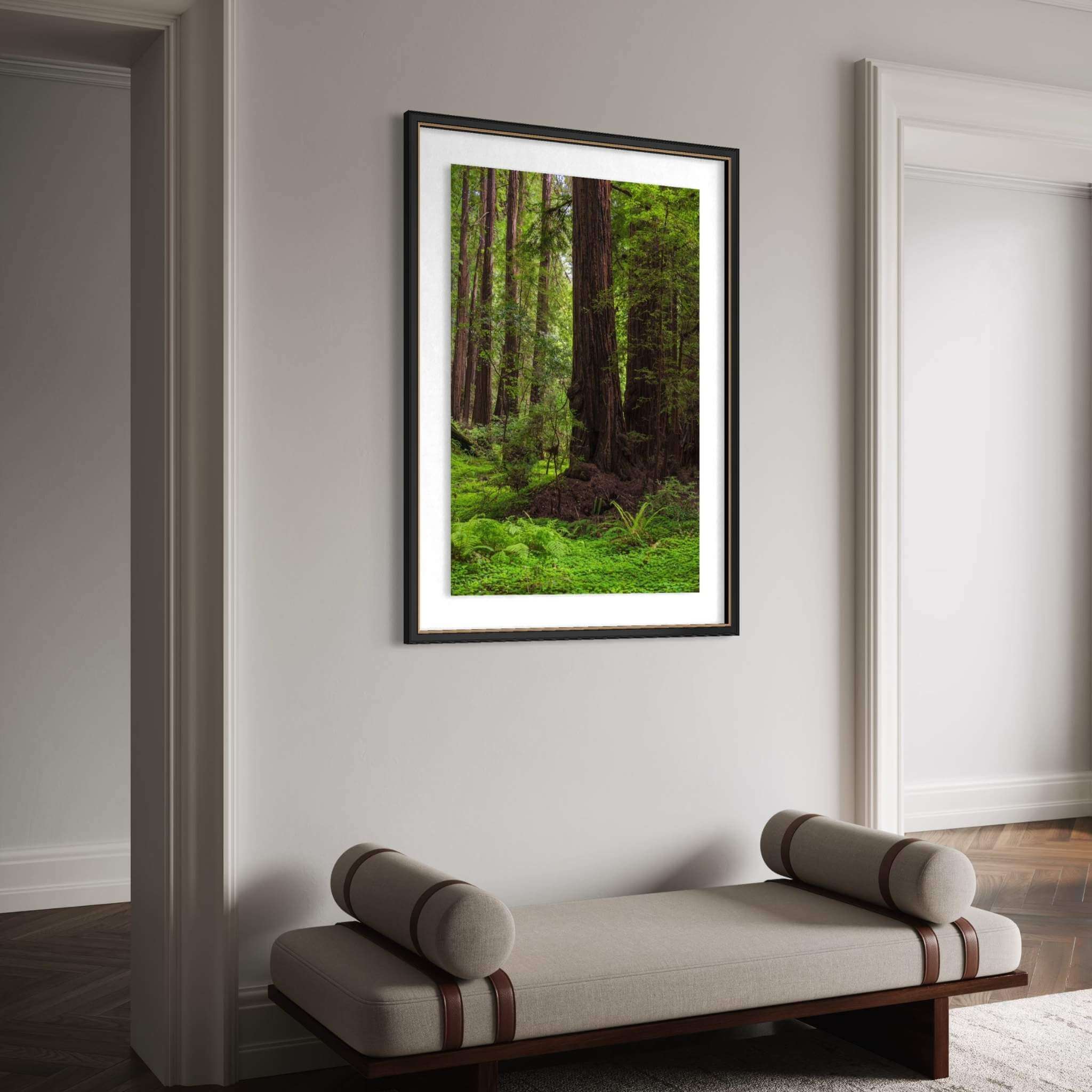 Ancient Stillness Among the Redwoods framed California redwood forest wall art by Abigail Diane Photography displayed in a refined modern entryway with a charcoal wood frame, upholstered bench with leather accents, dark herringbone wood flooring, and soft neutral walls, creating an elegant, nature-inspired luxury interior.