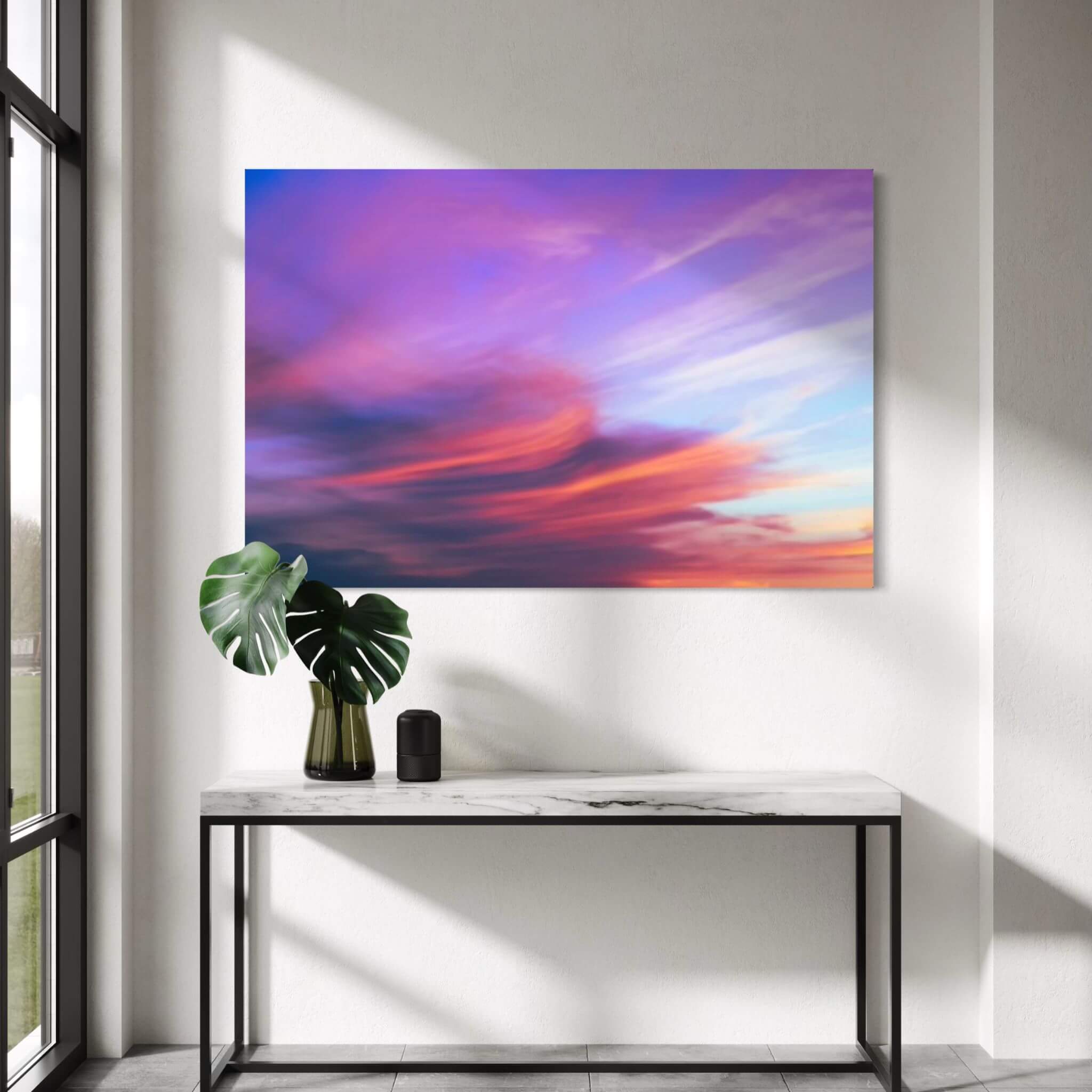 Lavender Dreams HD metal print displayed above a modern console table in a bright home office or entryway, featuring sweeping lavender, coral, pink, and blue sunset clouds by Abigail Diane Photography.