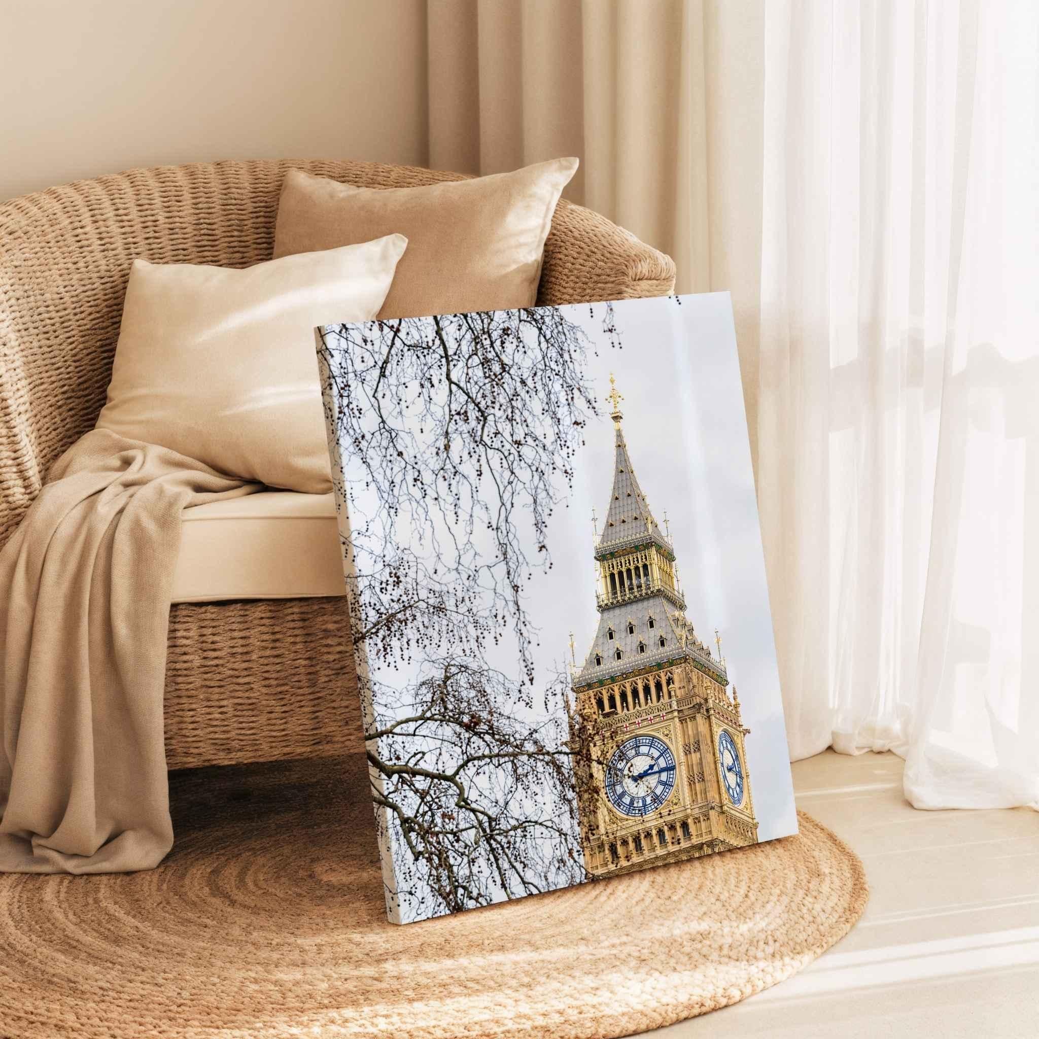Gallery wrapped canvas print of the restored Big Ben clock tower in London displayed leaning against a woven lounge chair in a warm neutral reading nook with soft linen cushions and natural sunlight, showcasing premium canvas wall art by Abigail Diane Photography.