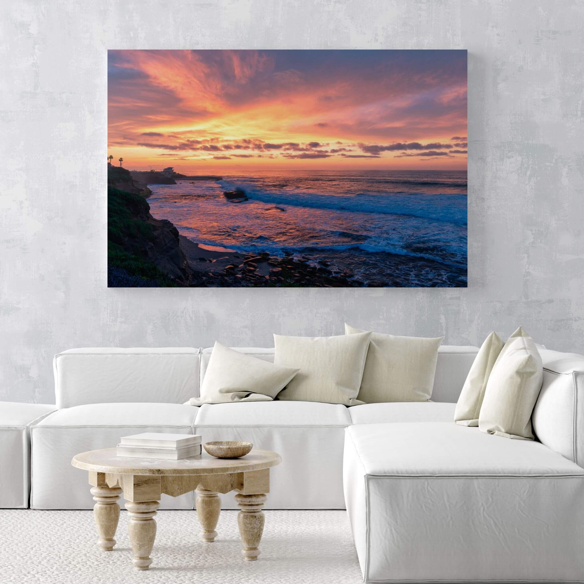 Candy Floss Sunset metal print displayed above a white sectional sofa, bringing pink, peach and blue coastal color into a contemporary living room.