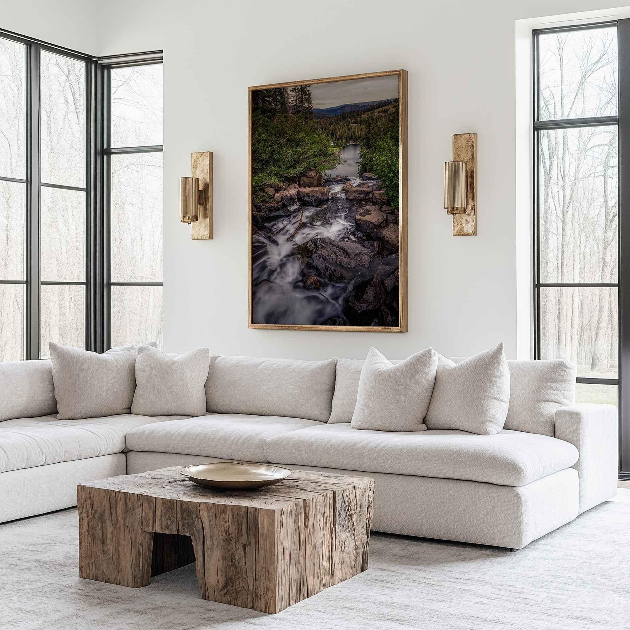 Cascading Into Stillness fine art print displayed in a natural wood frame above a white sofa, featuring a cascading mountain stream flowing toward a peaceful lake in California’s Eastern Sierras.