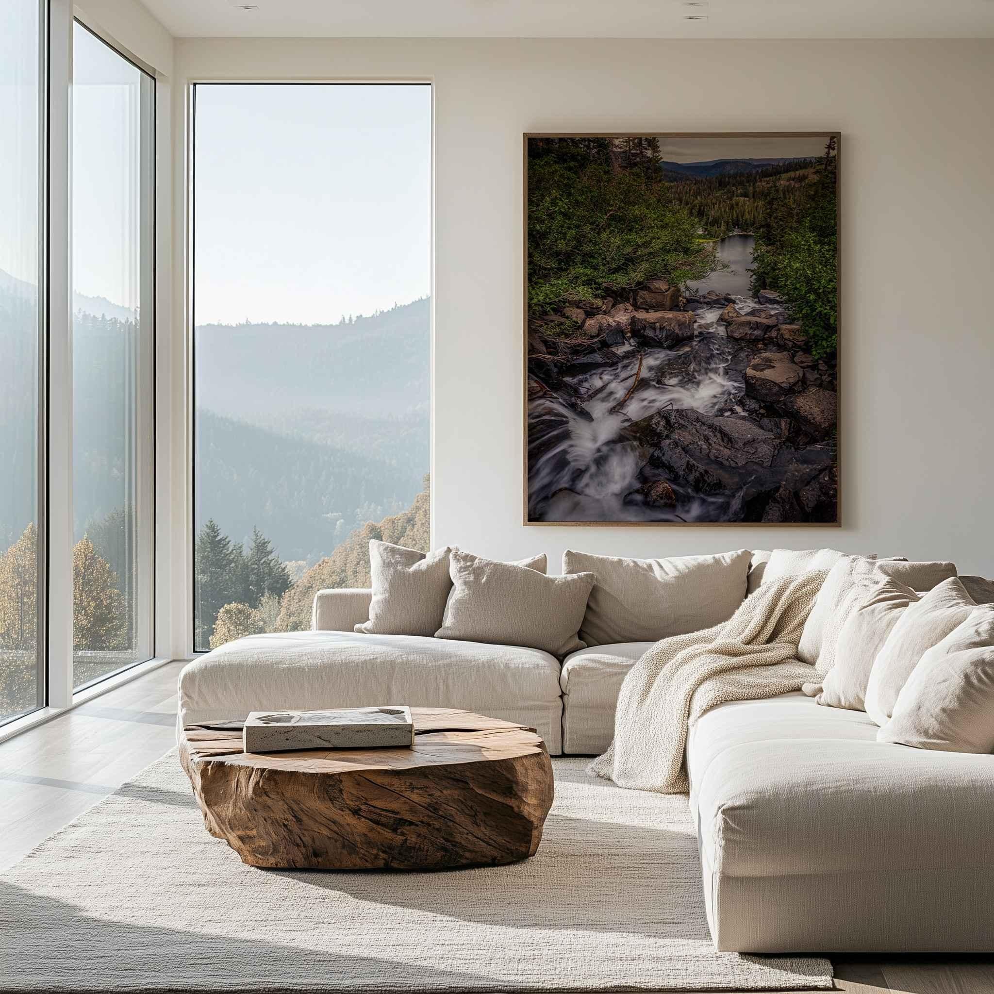 Cascading Into Stillness fine art print displayed in a natural wood frame above a white sofa in a mountain-view living room, featuring a cascading stream flowing toward a peaceful lake in California’s Eastern Sierras.