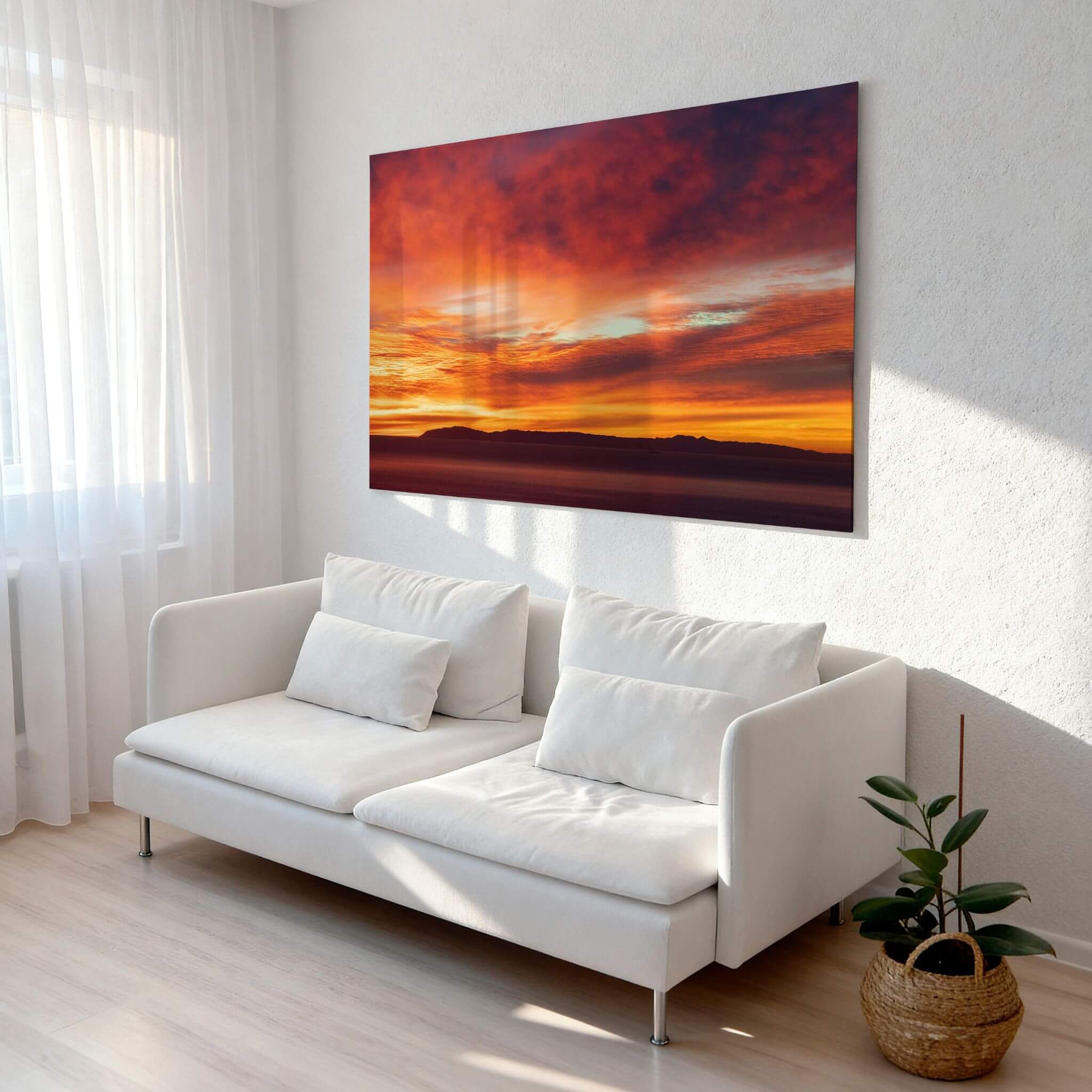 Catalina Beneath Crimson Skies metal print displayed above a white sofa in a sunlit modern living room, showcasing rich crimson and orange sunset tones. Photography by Abigail Diane Photography.